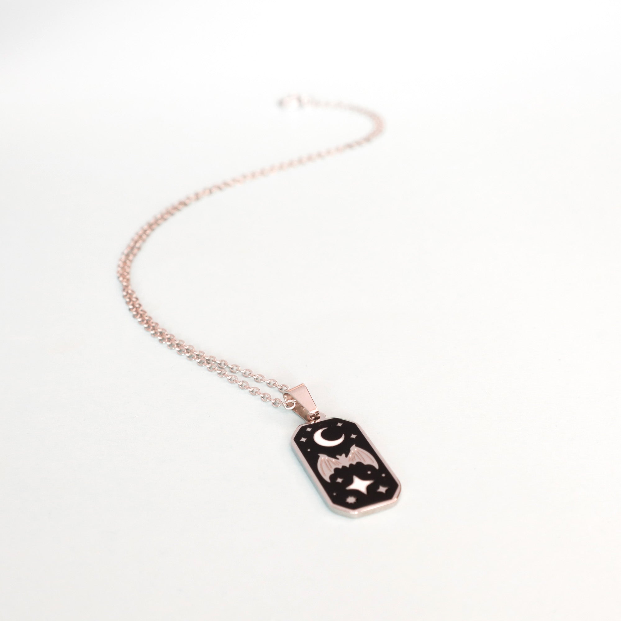 The Papio Press Bat & Moon Enamel Necklace features a delicate rose gold chain and a rectangular pendant engraved with a bat, stars, and crescent moon, shown on a plain white background.