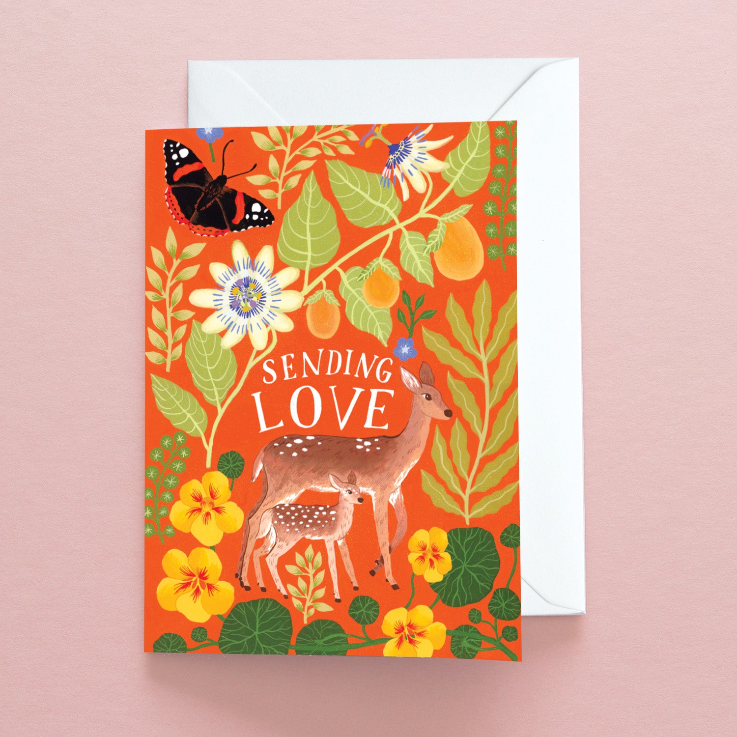The Papio Press Sending Love Deer Greetings Card has an orange background, deer and fawn, yellow flowers, green leaves, a butterfly, and Sending Love in white. Includes a white envelope; printed on recycled stock.