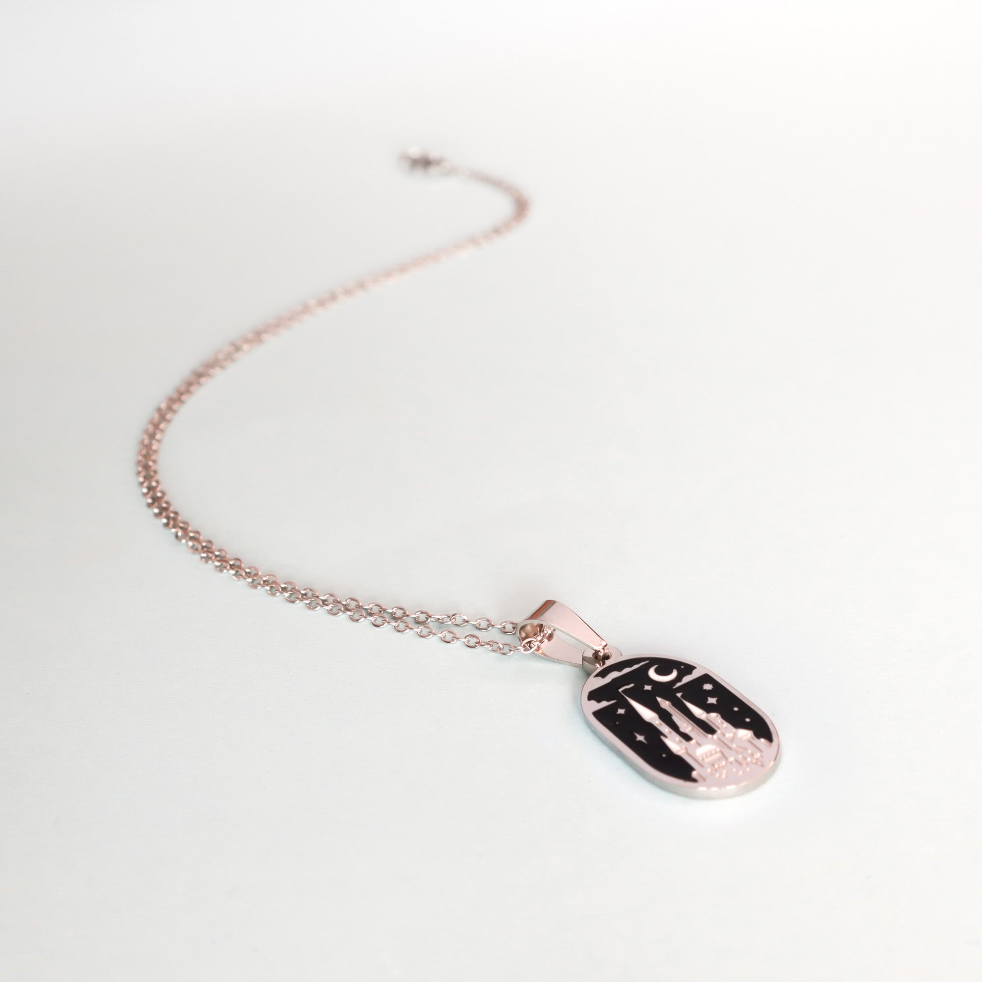 The Papio Press Moonlit Castle Enamel Necklace features a rectangular pendant engraved with a castle, crescent moon and stars against a black background, displayed on a white surface.