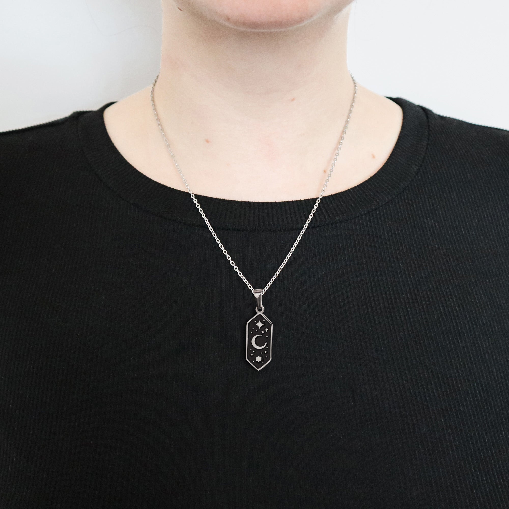 A person wears a black ribbed shirt and the Papio Press Crescent Moon Pendant Enamel Necklace, featuring gold plating with star details. The image is cropped to show only the neck and upper chest.