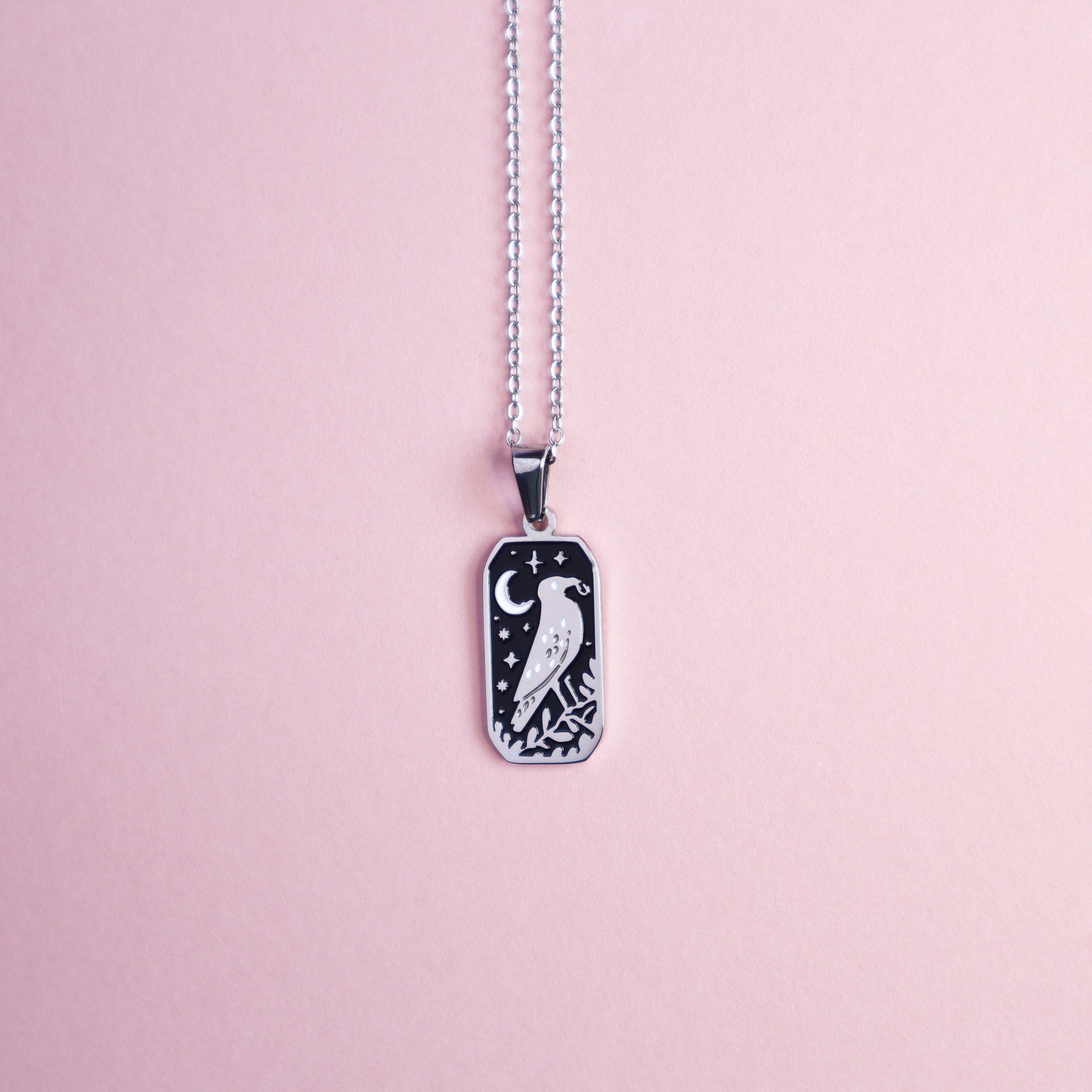 The Crow and the Ring Pendant Enamel Necklace by Papio Press features a silver crow, crescent moon, and stars engraved on a black rectangular enamel pendant—an enchanting piece of fantasy jewelry.