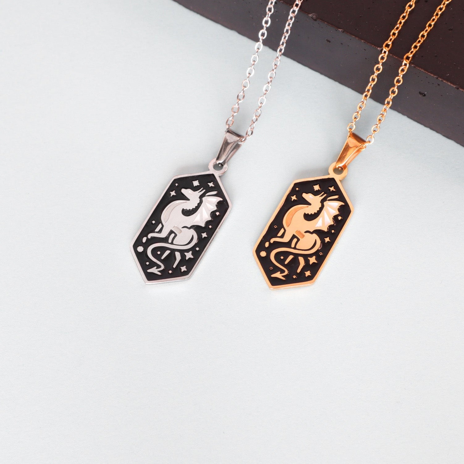 A Papio Press Dragon Pendant Enamel Necklace rests on a white surface beside a dark rectangular object.