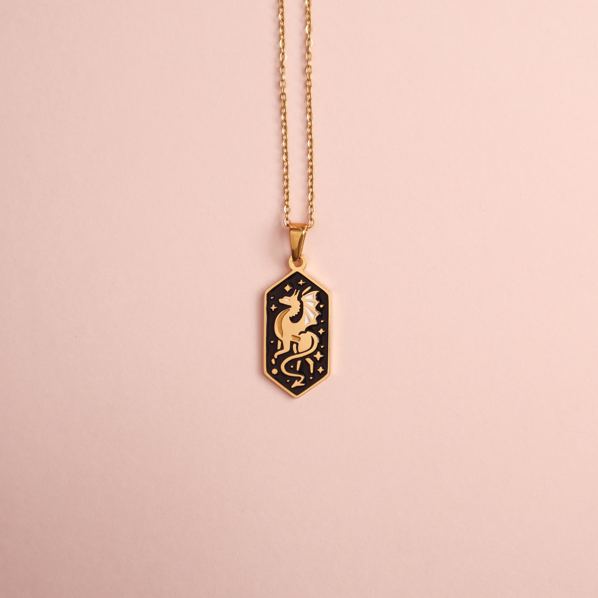 The Papio Press Dragon Pendant Enamel Necklace features an 18K gold-plated hexagonal black charm with a gold dragon and star design, displayed against a pale pink background.