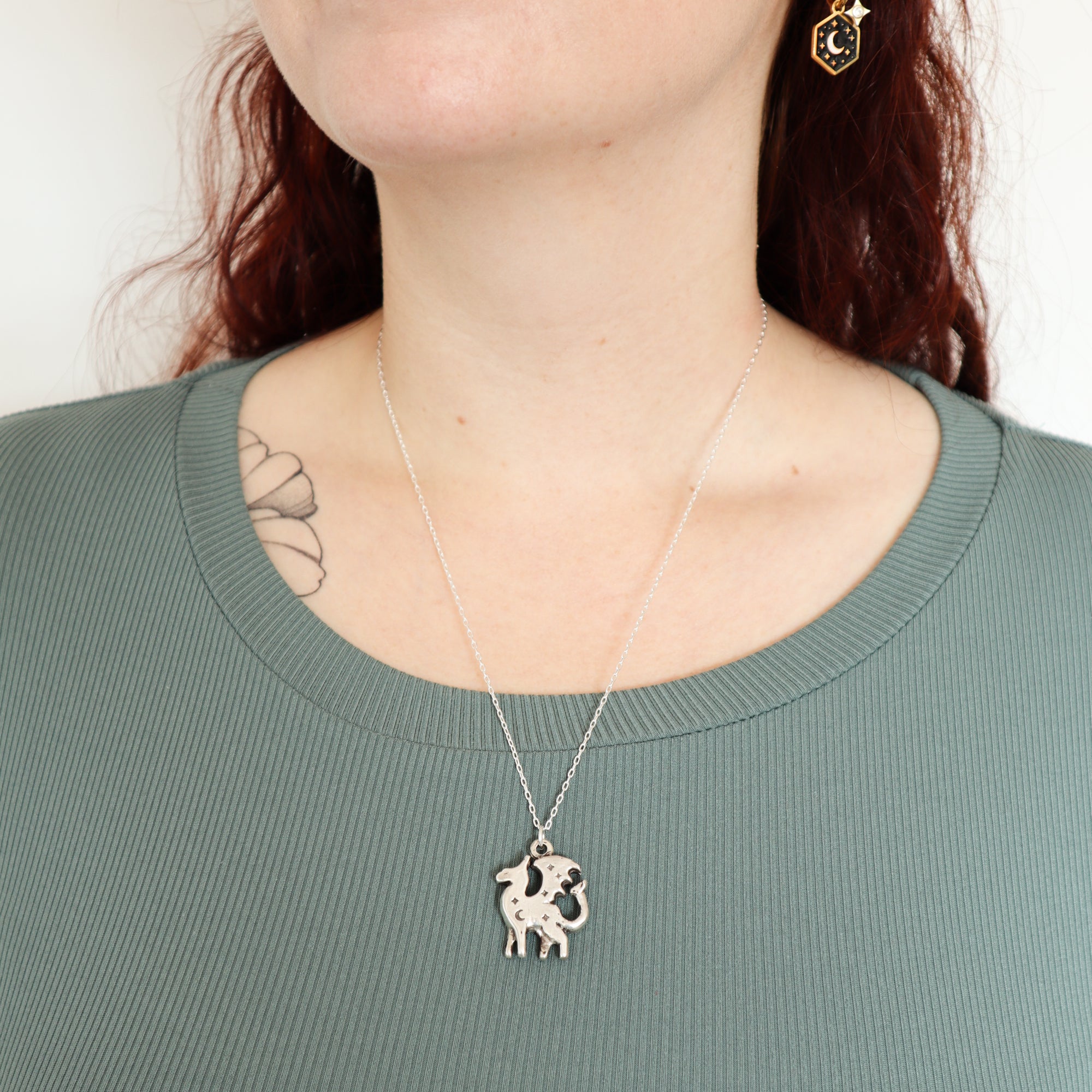 A person with wavy, red hair wears a ribbed, sage-green top, handmade silver jewelry, a Papio Press Silver Lunar Dragon Pendant.
