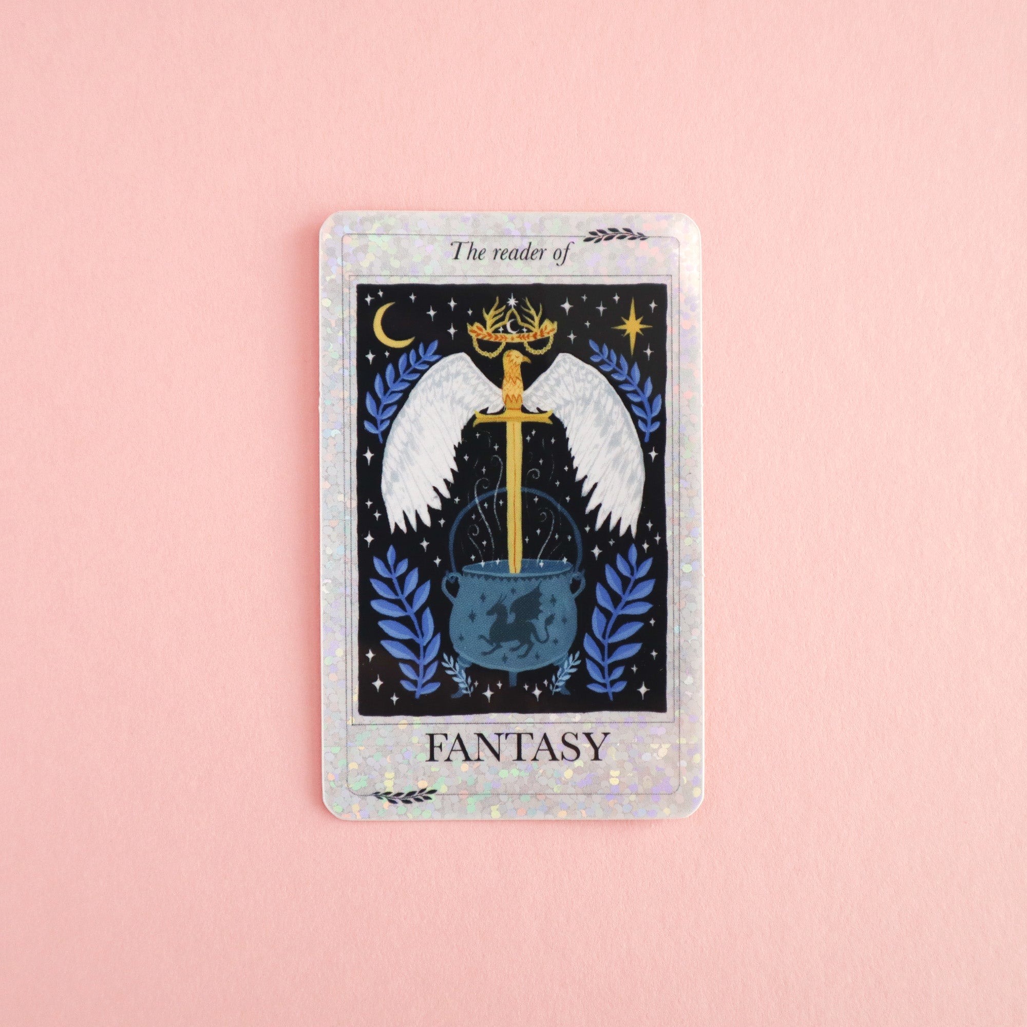 The Reader of Fantasy Sticker by Papio Press shows a sword with white wings, a gold crown, and a cauldron on pink, surrounded by blue leaves under the title The Reader of Fantasy. Ideal as a glitter or vinyl sticker for your collection.