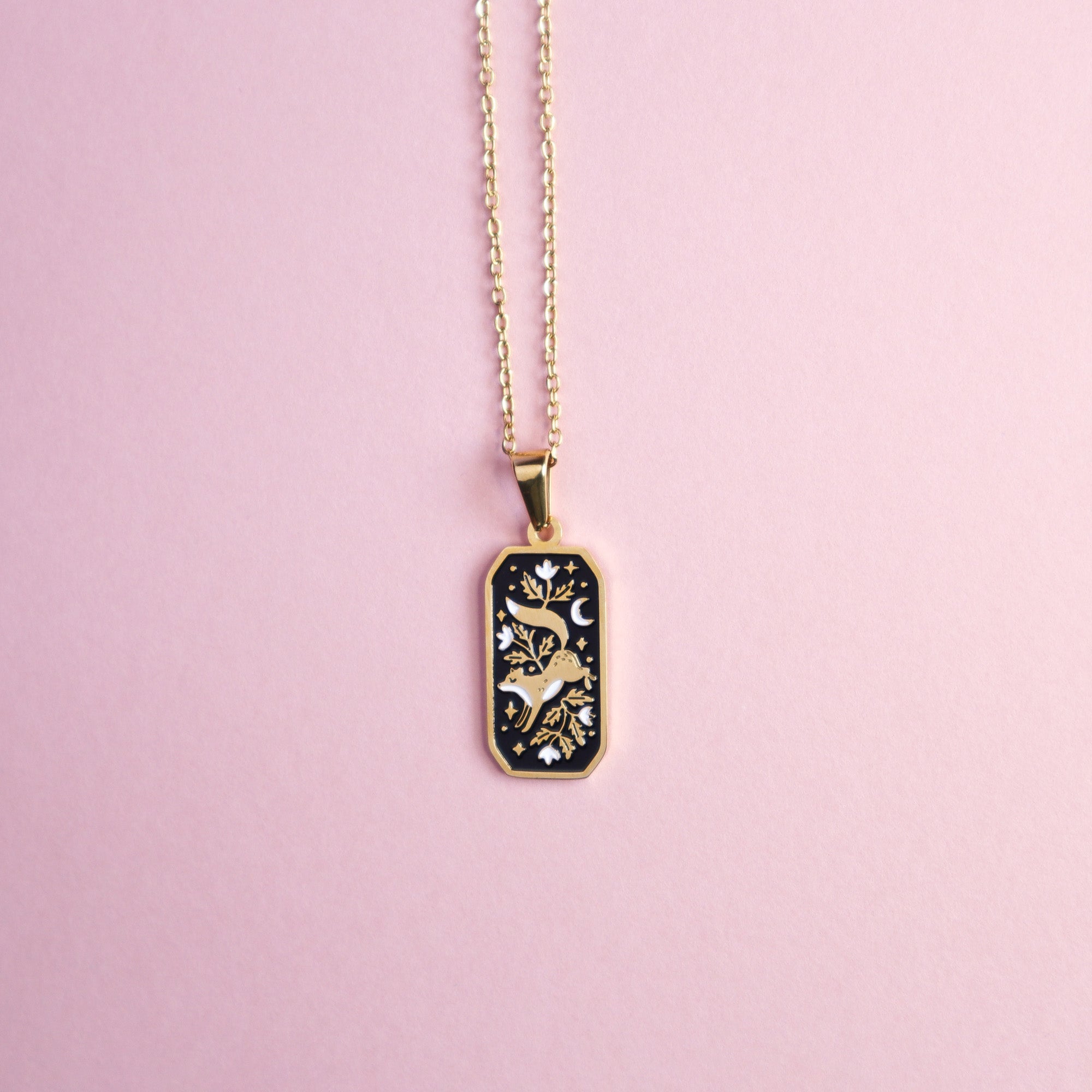 A gold floral fox necklace taken a on light pink surface.