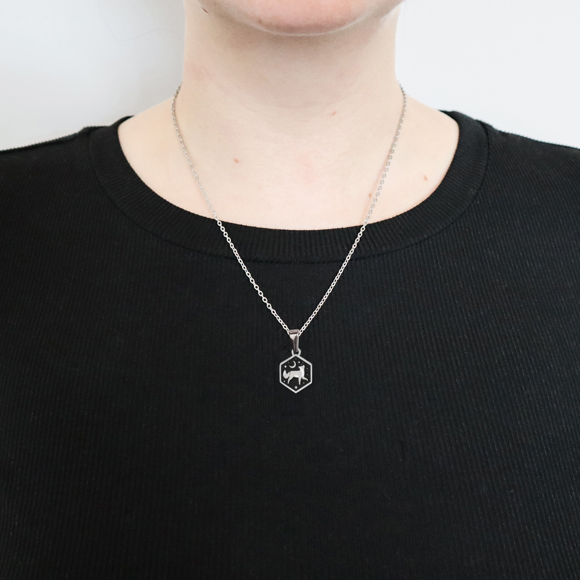 A person wearing a black ribbed shirt and a Papio Press Mini Hexagon Fox Pendant in stainless steel. The image is cropped below the nose, highlighting the necklace.