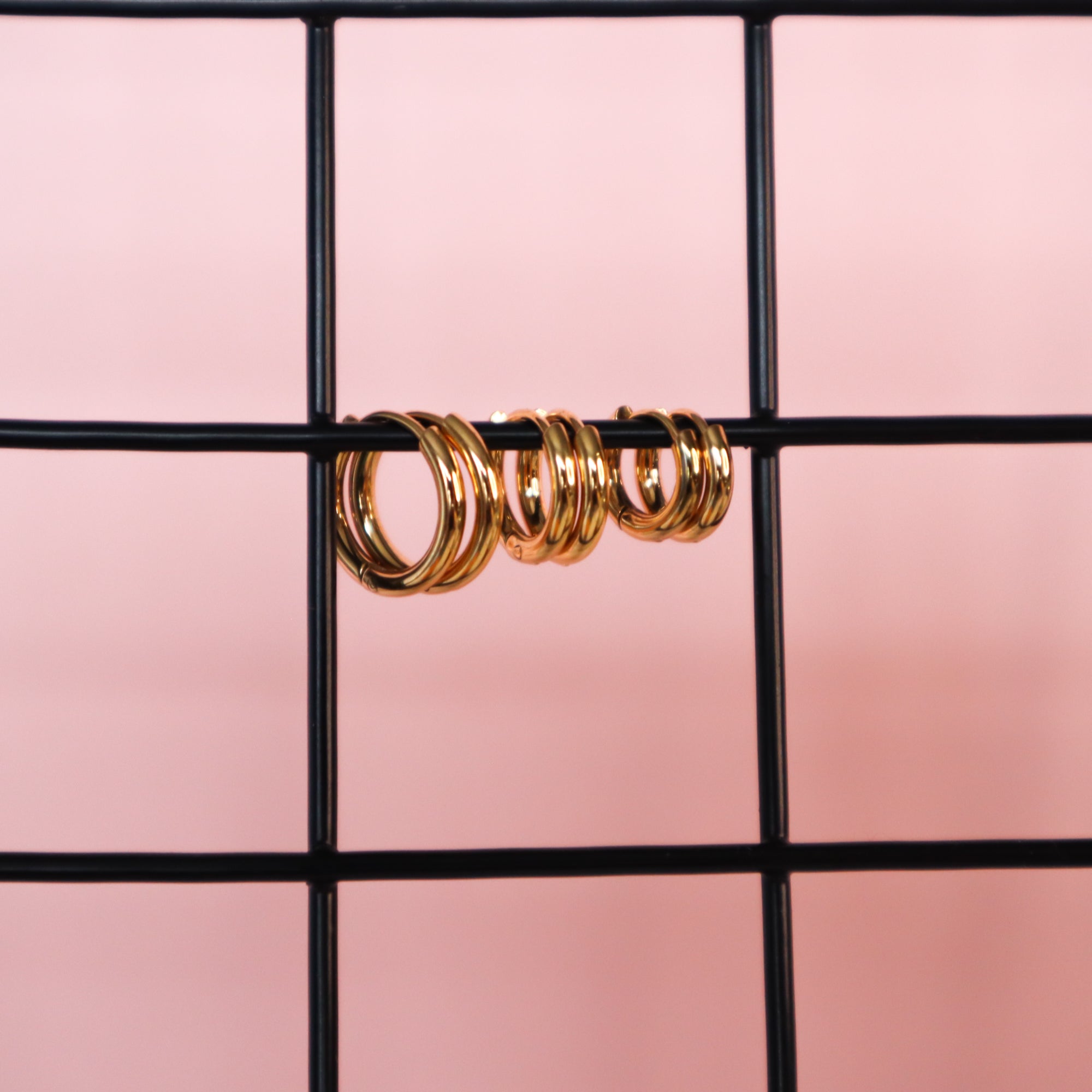 3 pairs of gold huggie hoop earrings hanging on a black wire.