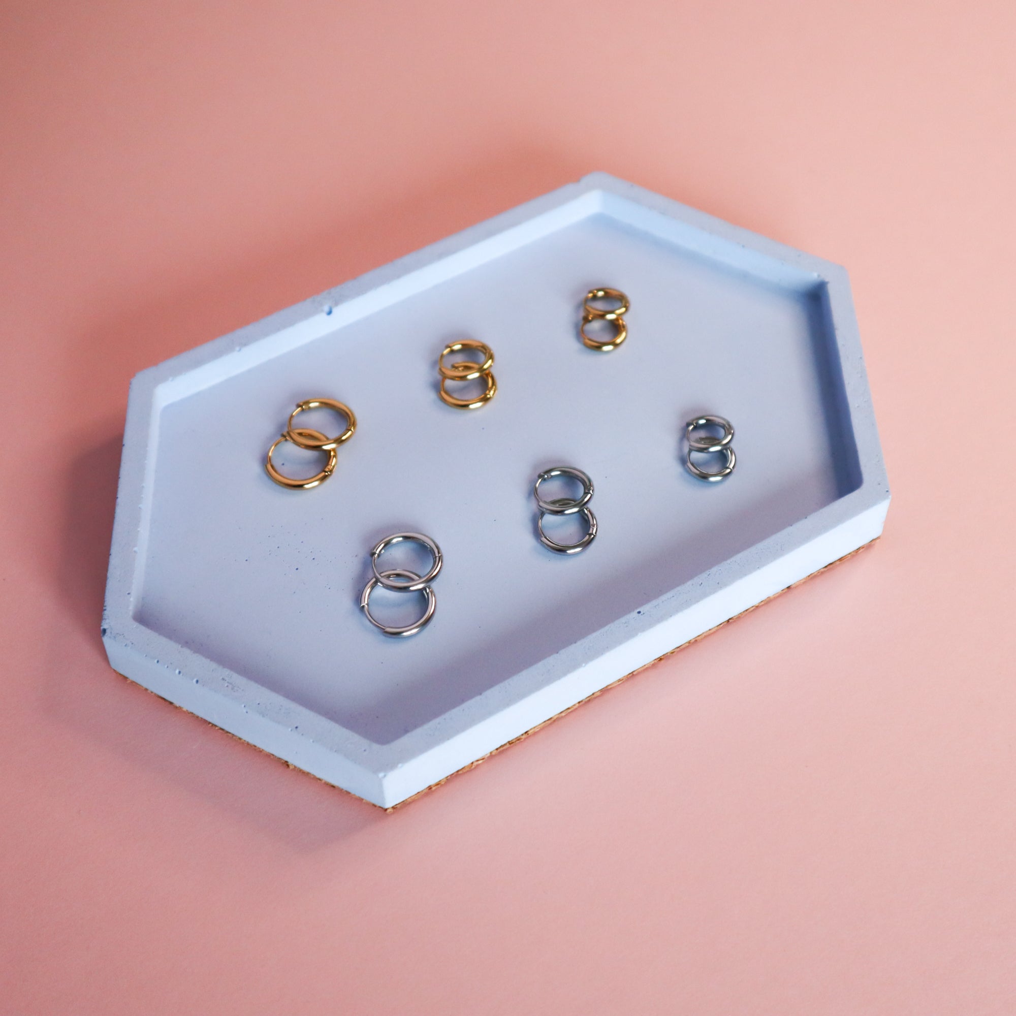 6 pairs of gold and silver huggie hoop earrings on a blue concrete tray.