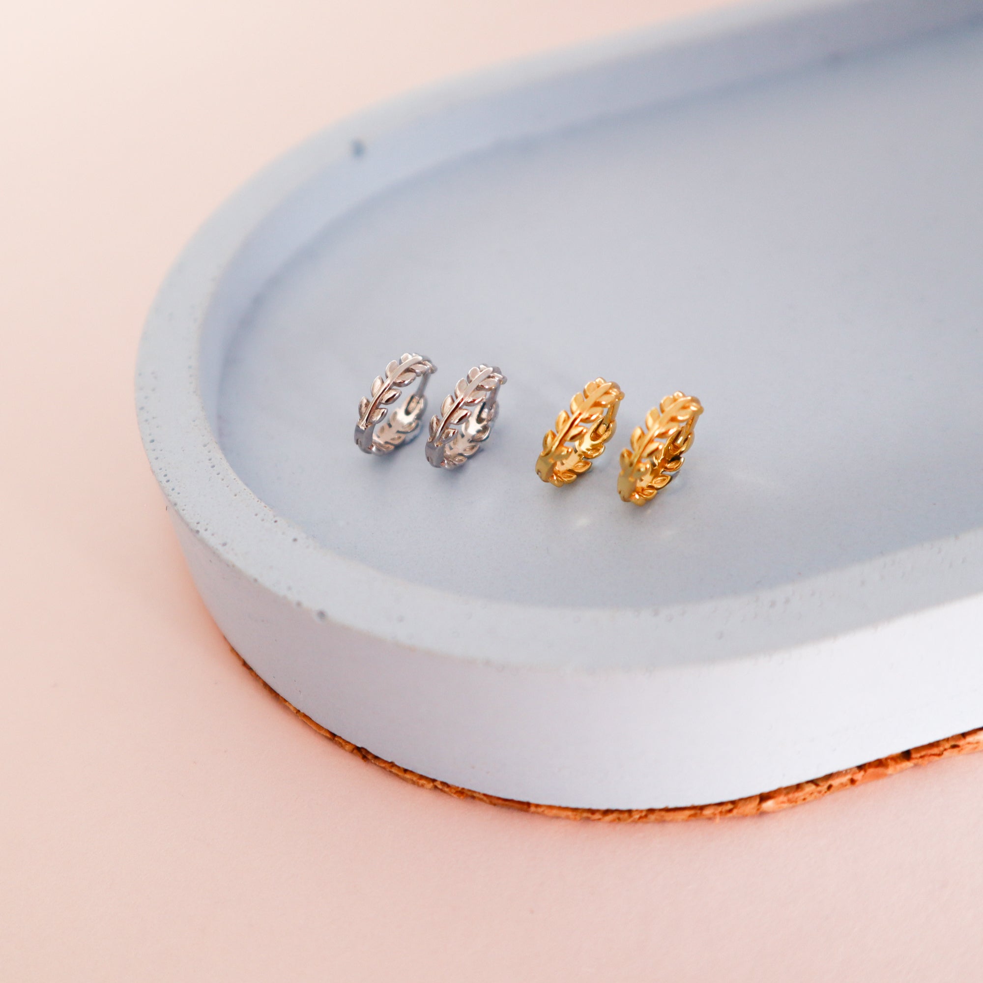 Two pairs of leafy laurel hoops, one gold and one silver. They have leaf shaped hoop with a clip mechanism.