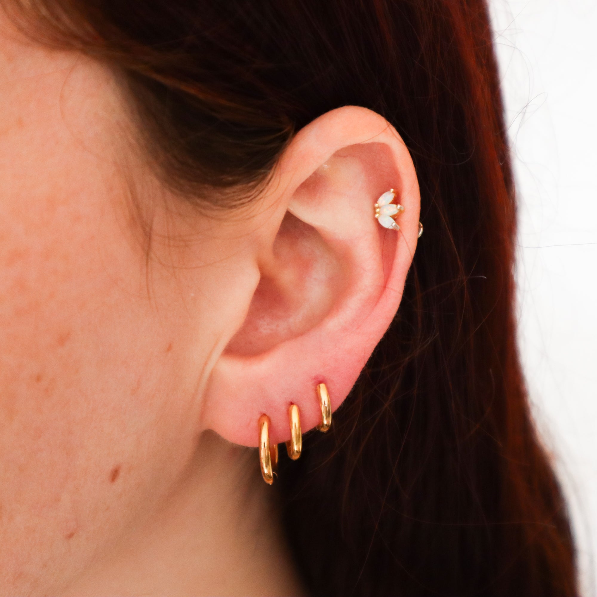 A woman's ear with 3 different sized gold huggie hoops, one 8mm, one 10mm and one 12mm.