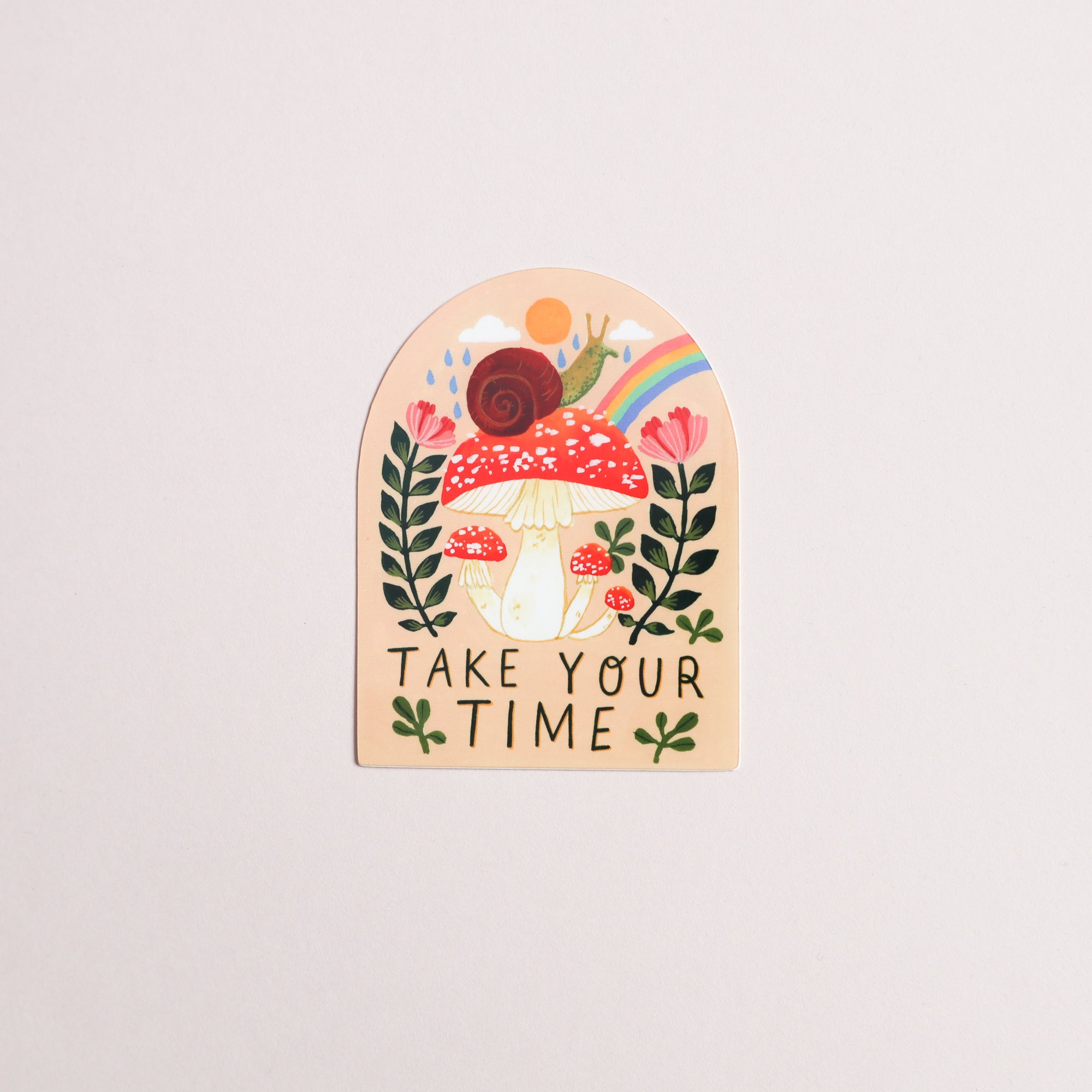 The Take Your Time Snail Sticker by Papio Press features a red and white mushroom, brown snail, flowers, leaves, a rainbow, and sun on a soft beige background with “TAKE YOUR TIME” below. Glossy finish with UV protection.