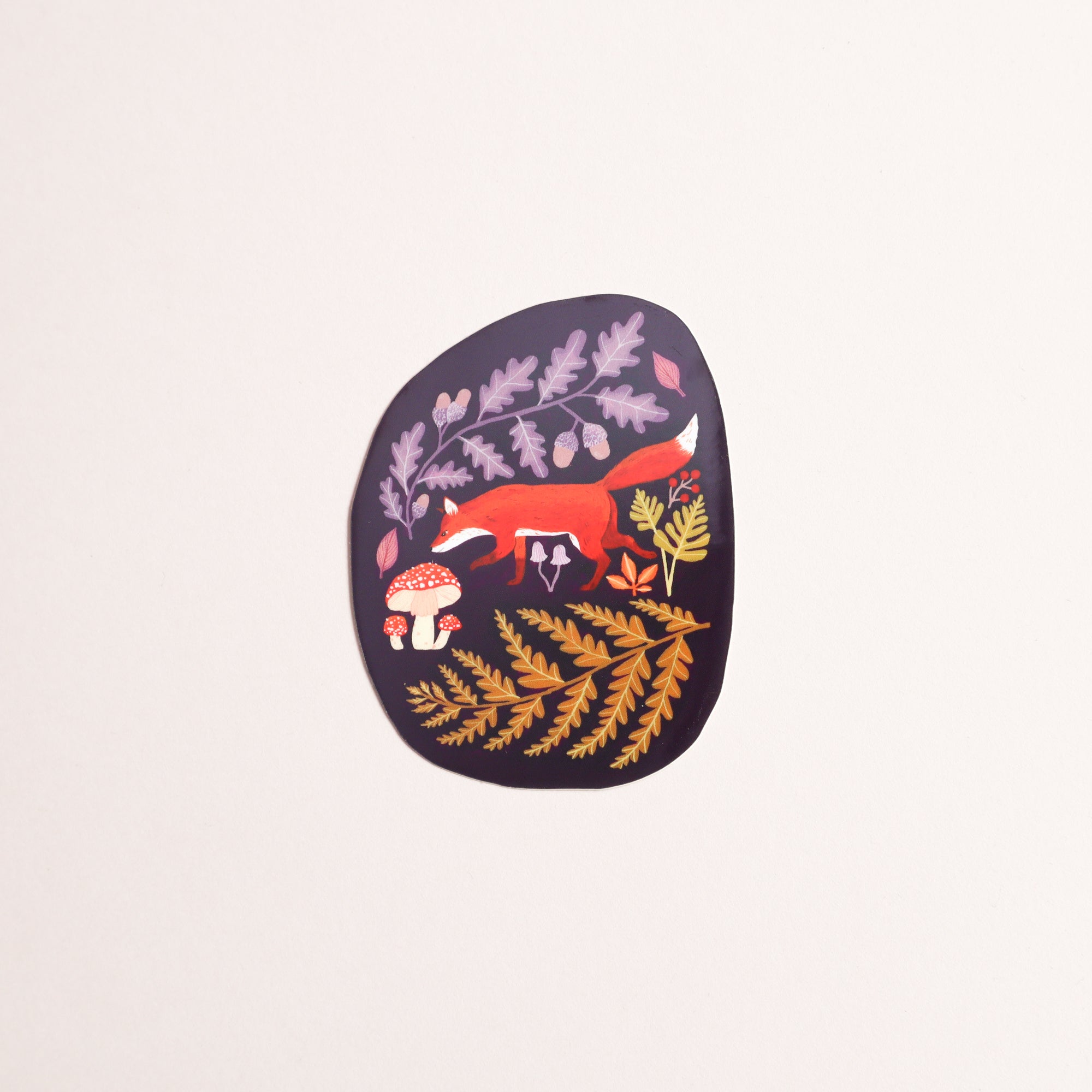 The Autumnal Fox Sticker by Papio Press is a round vinyl sticker with an autumn fox among ferns, leaves, and red mushrooms on a dark background. UV-protected for vibrant color indoors or out.