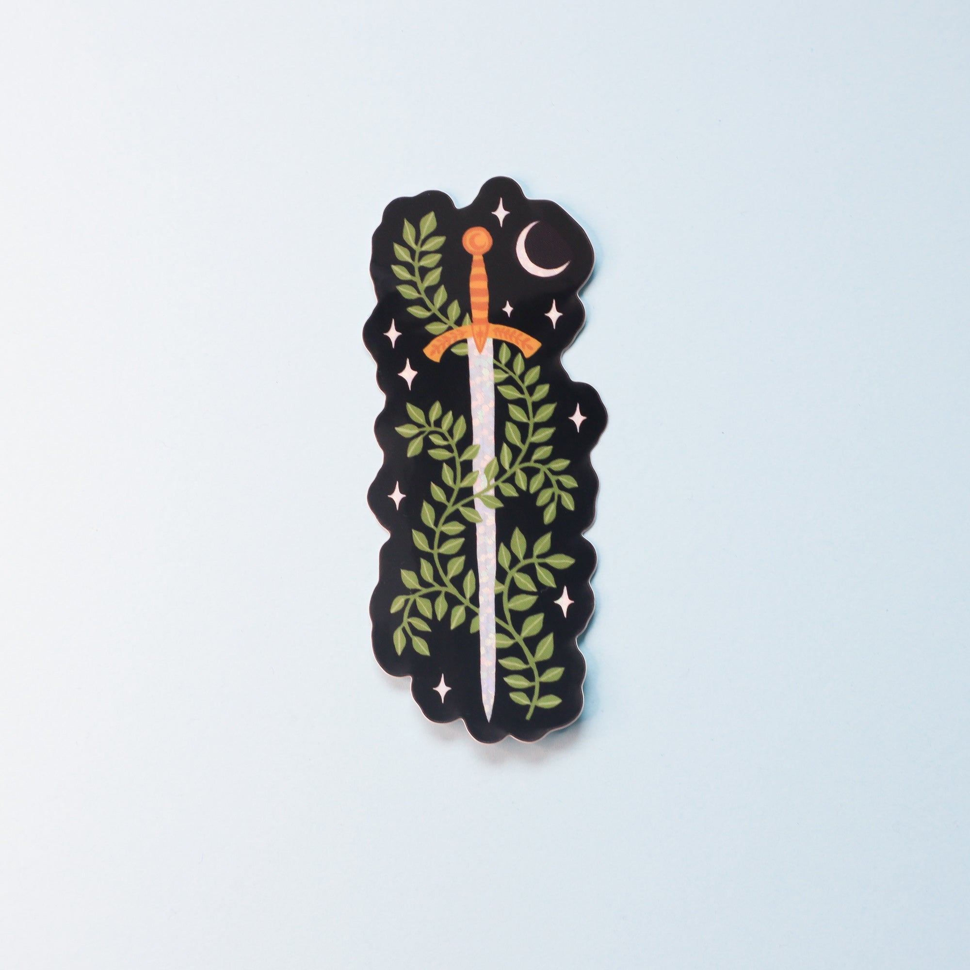 Part of the Papio Press Fantasy Sticker Collection, this glossy vinyl sticker features a gold-hilted sword entwined with green vines and leaves under a starry night sky with a crescent moon, offering UV protection.