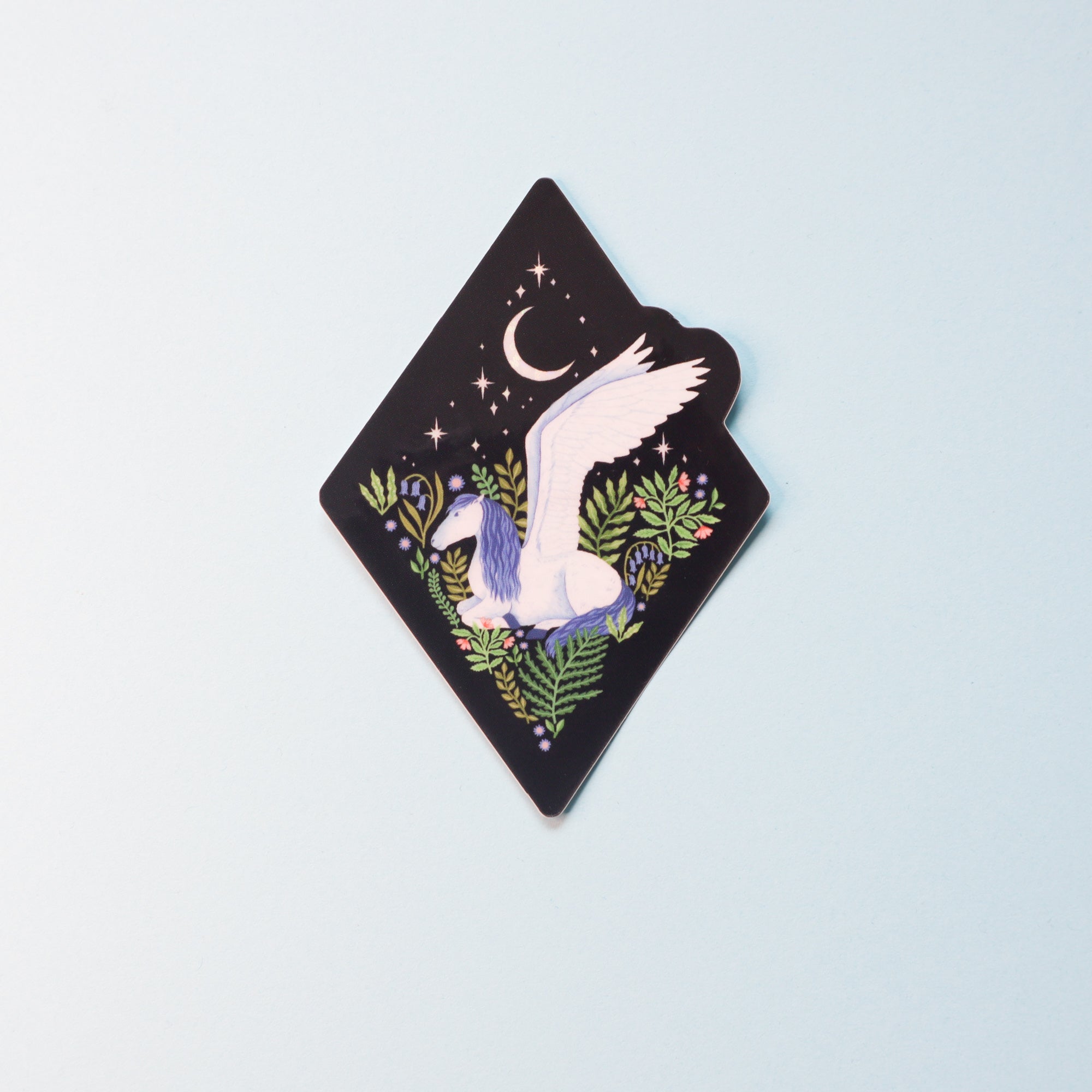 From the Papio Press Fantasy Sticker Collection: a diamond-shaped glossy vinyl sticker showing an illustrated white pegasus with blue and purple accents, leafy plants, and stars beneath a crescent moon on a pale blue background.