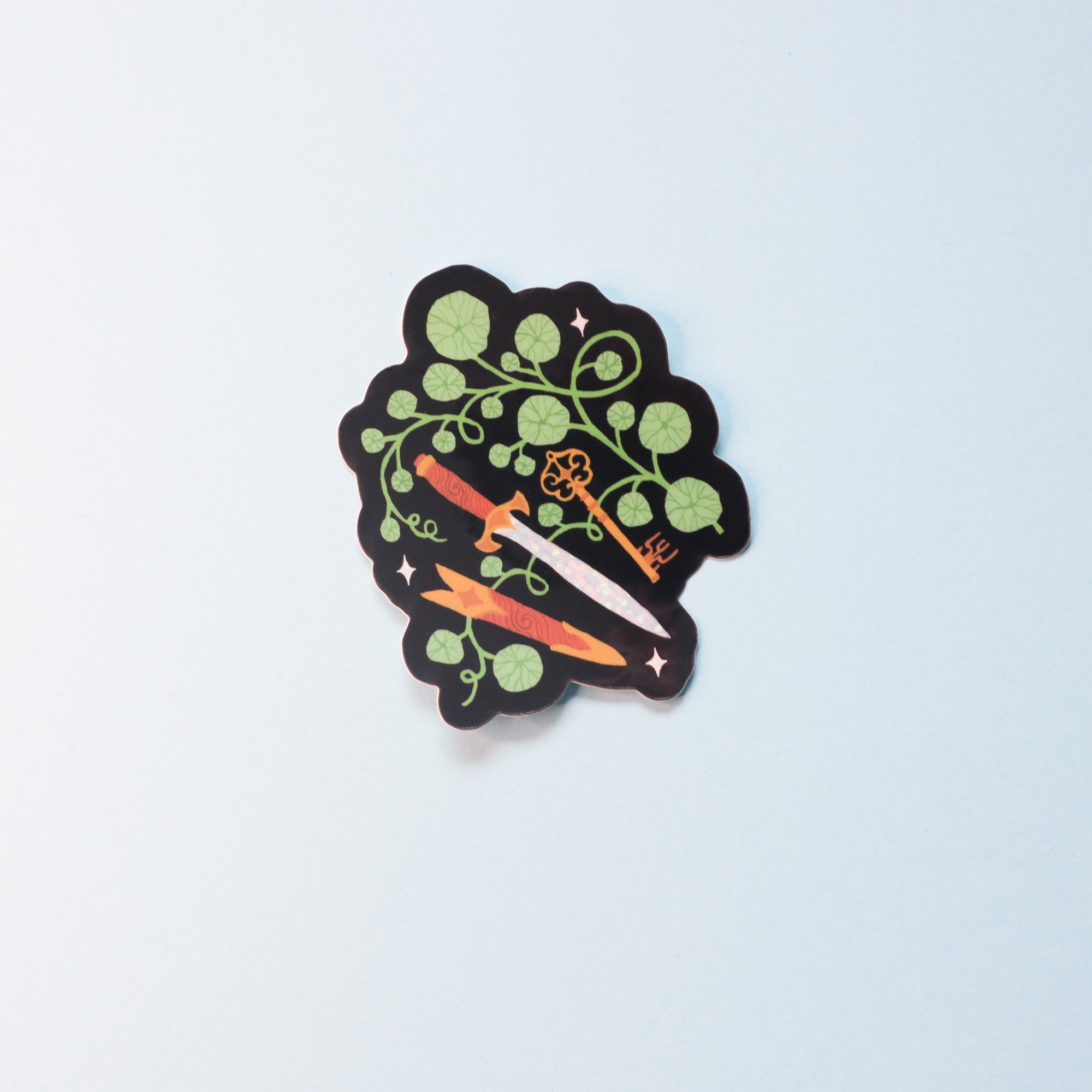 The Fantasy Sticker Collection from Papio Press features a glossy vinyl sticker with green leafy vines and two orange carrots on a black scalloped background, shown on a plain light surface.