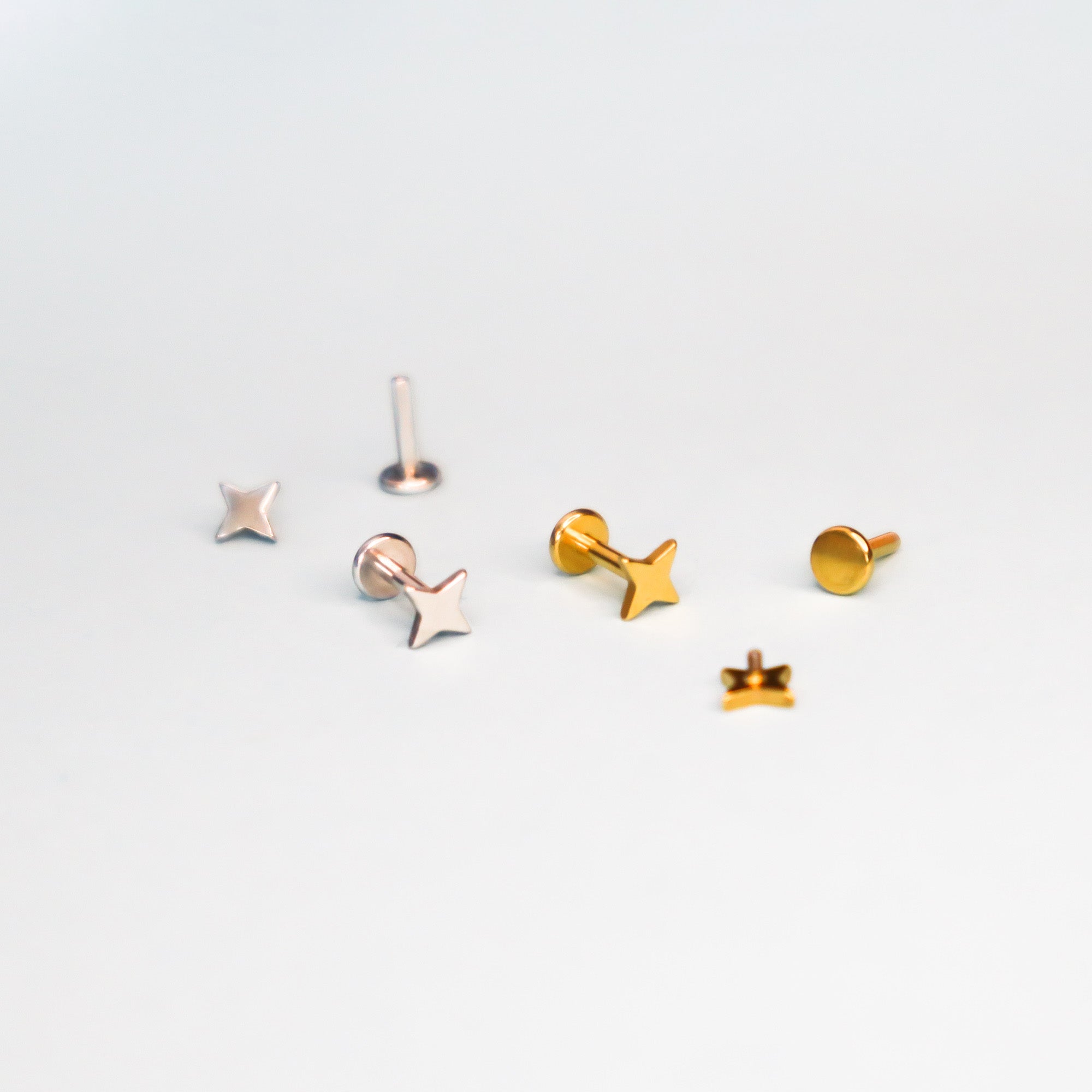 The Papio Press Star Labret Earring features small star and round studs in nickel-free gold and silver tones, ideal for cartilage piercings. Displayed on a plain white background.