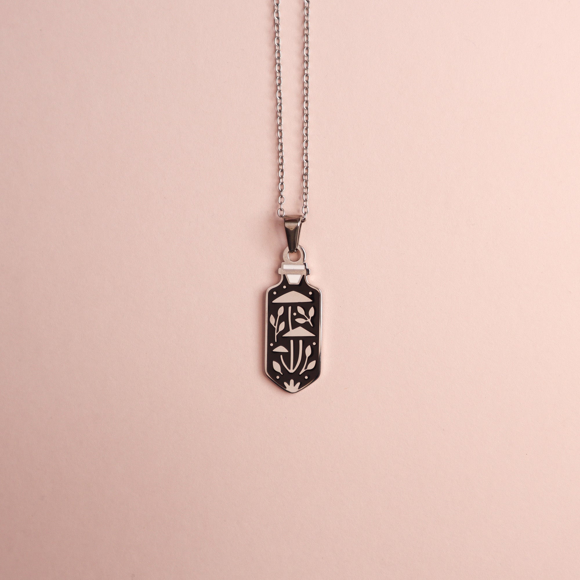 The Mushroom Potion Pendant Enamel Necklace by Papio Press features an intricate geometric and floral design, showcased on a light pink background.