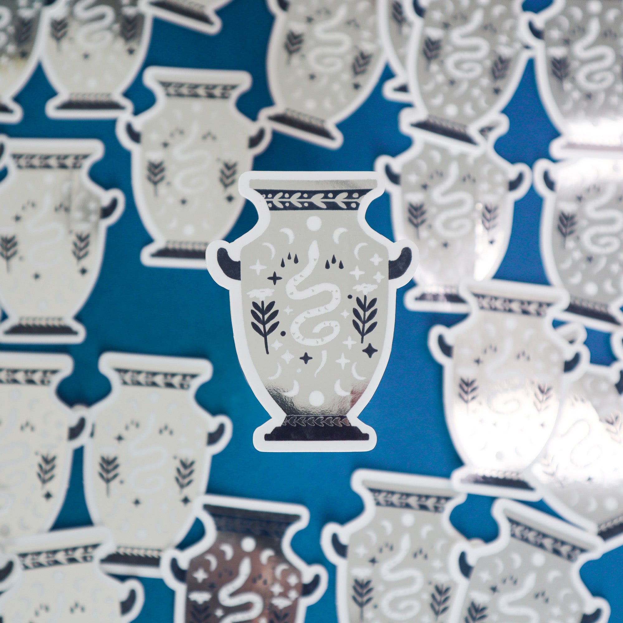 Papio Press’s Set of Three Unicorn, Dragon & Snake Vase Stickers features illustrated designs on a blue background; a metallic-finished dragon sticker is centered in focus, with the other stickers slightly blurred in the background.