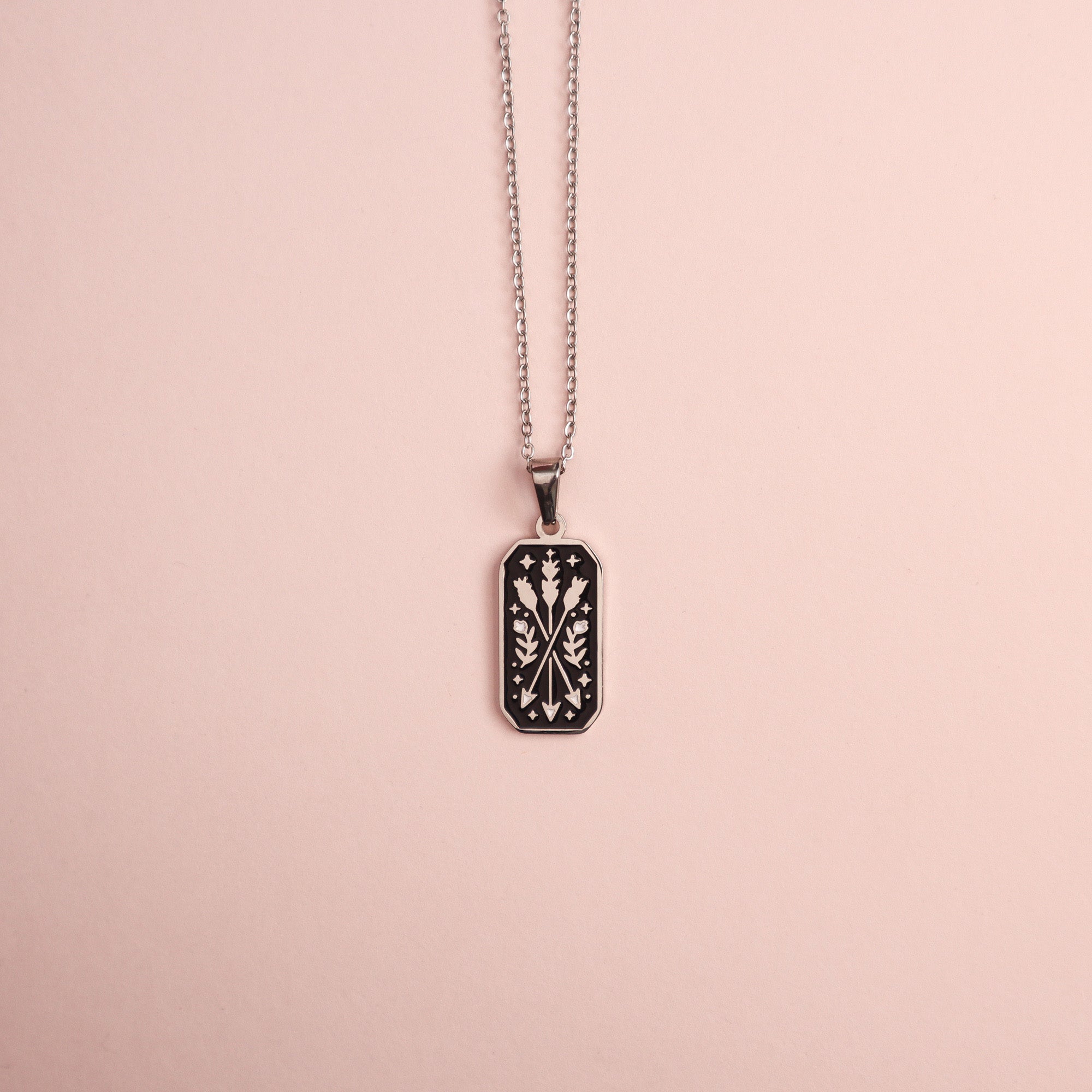 The Ranger Pendant Enamel Necklace by Papio Press features a silver chain with a rectangular black pendant, decorated with a white symmetrical botanical design, making it an enchanting piece for fantasy lovers.