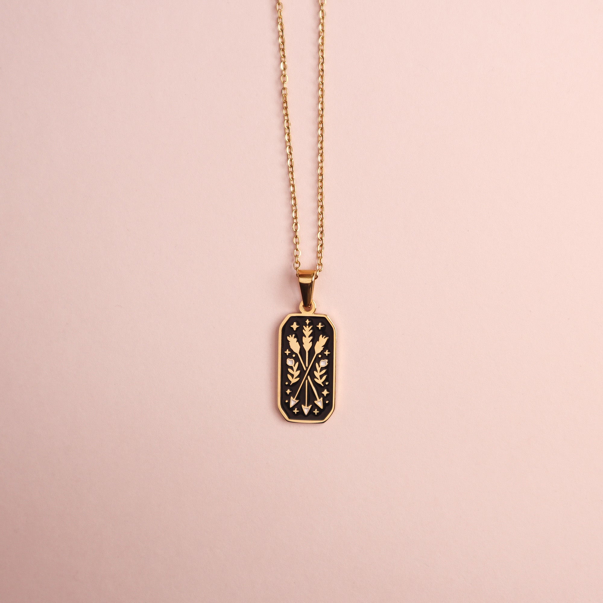 The Ranger Pendant Enamel Necklace by Papio Press features a gold-plated rectangular pendant with an intricate black enamel floral design, ideal for fantasy lovers, shown on a light pink background.