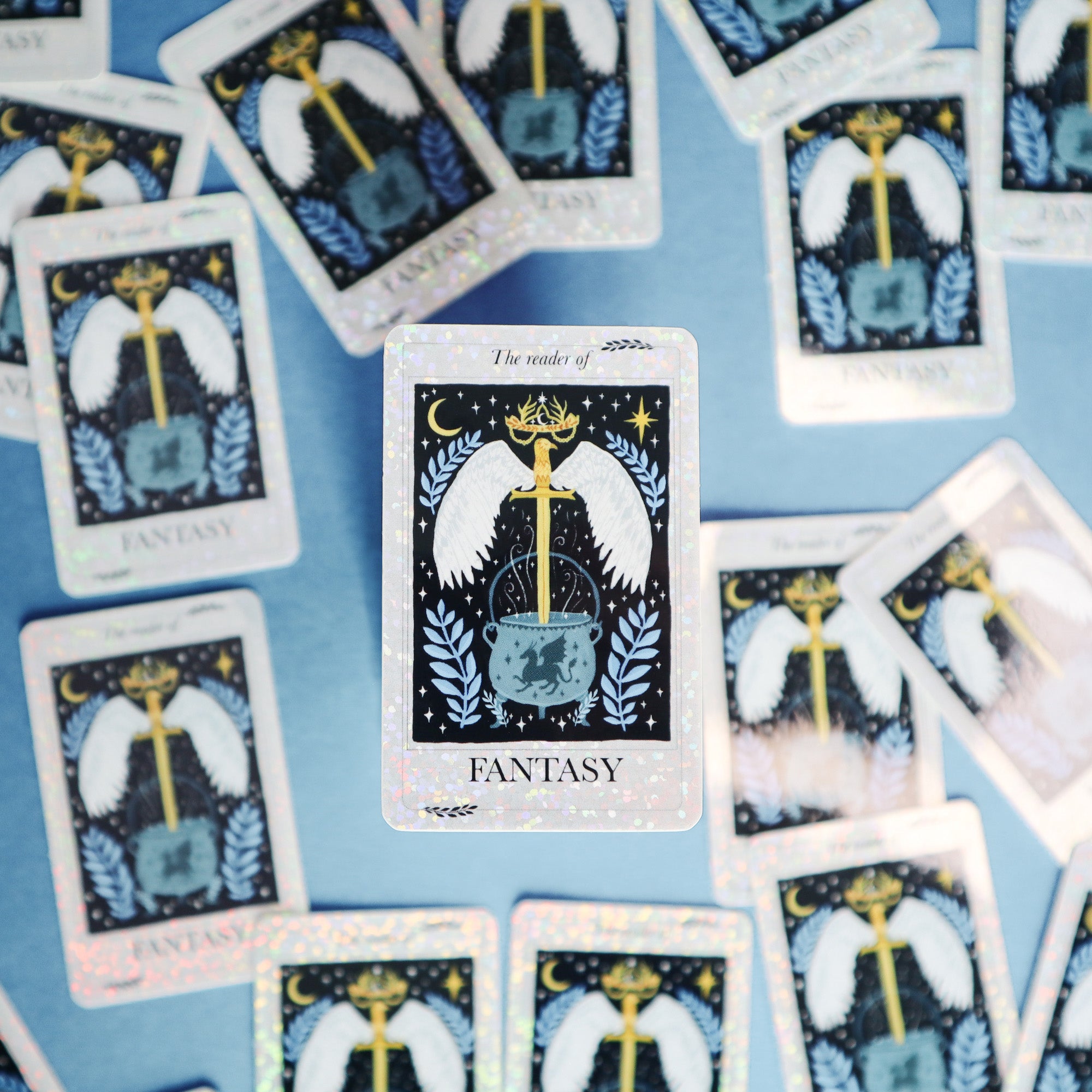 The Reader of Fantasy Sticker by Papio Press features a tarot card with a sword, wings, crown, and cauldron at its center among scattered cards—ideal as a fantasy or vinyl sticker with a glitter finish.