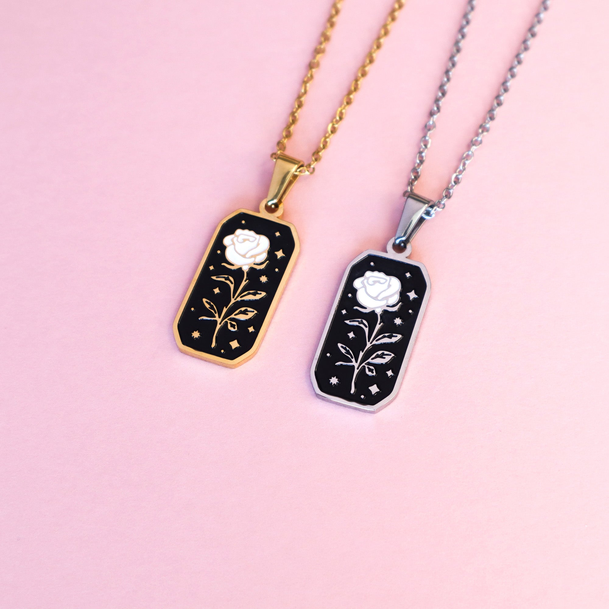 Two Papio Press Rose necklaces, one gold and one silver. The pendant is rectangular and features a rose with black and white enamel details on a light pink surface.