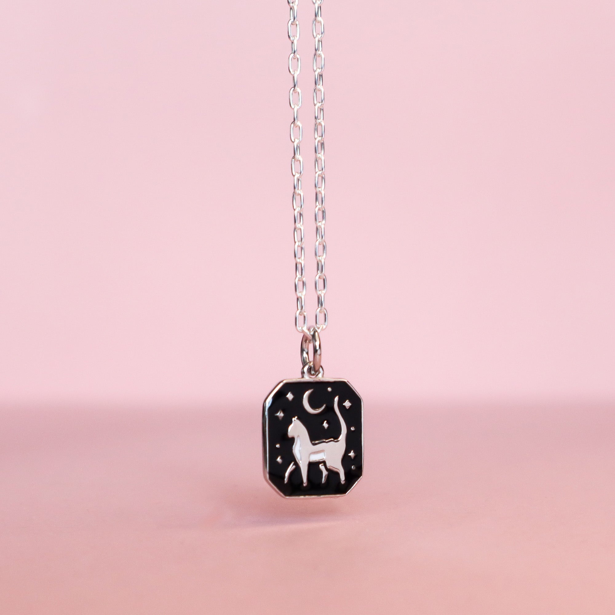 The Papio Press Silver Cat Pendant Enamel Necklace features a rectangular black cat design and is displayed against a soft pink background.