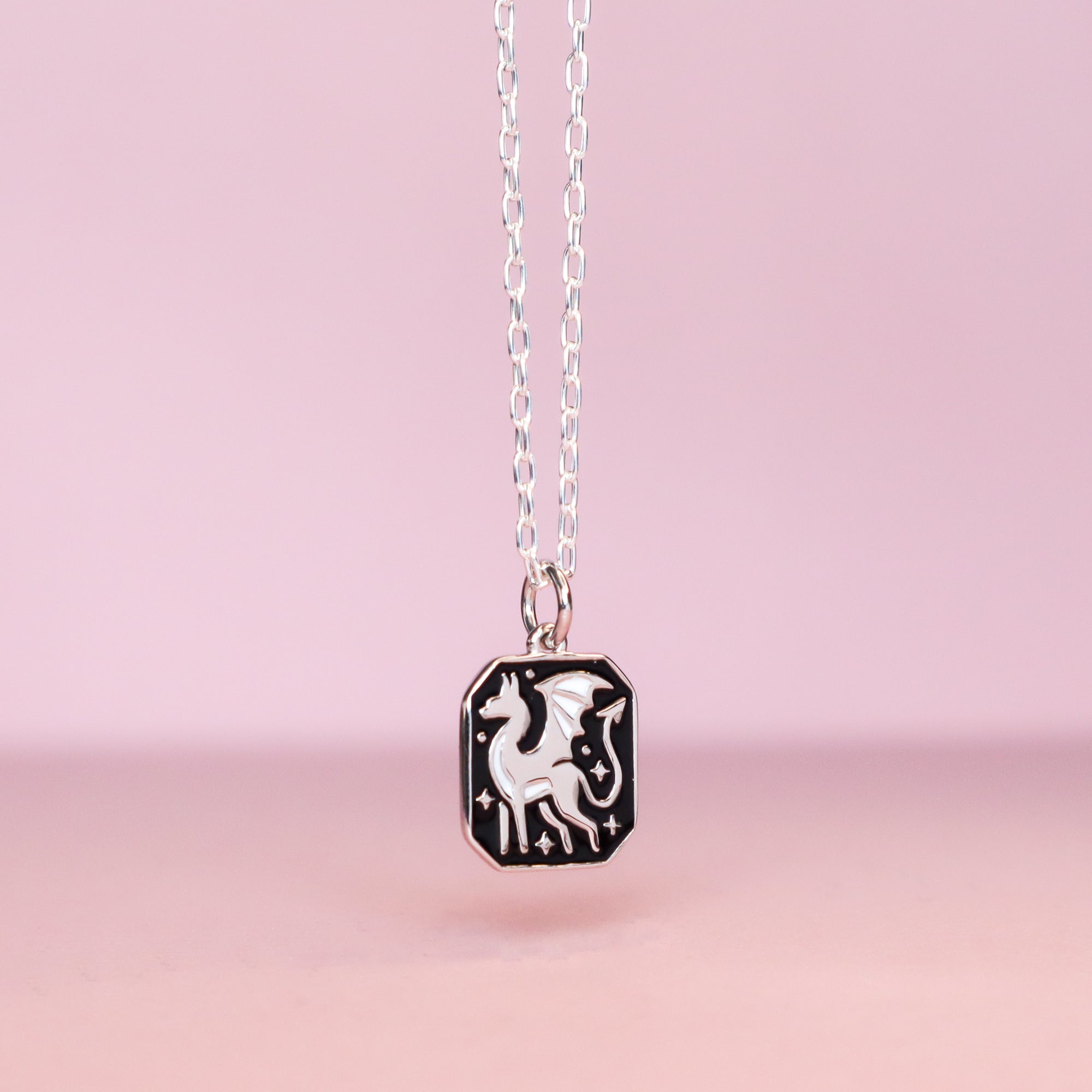 The Silver Dragon Pendant Enamel Necklace by Papio Press showcases a rectangular black enamel pendant with a white dragon design, crafted from recycled silver and set against a soft pink background.