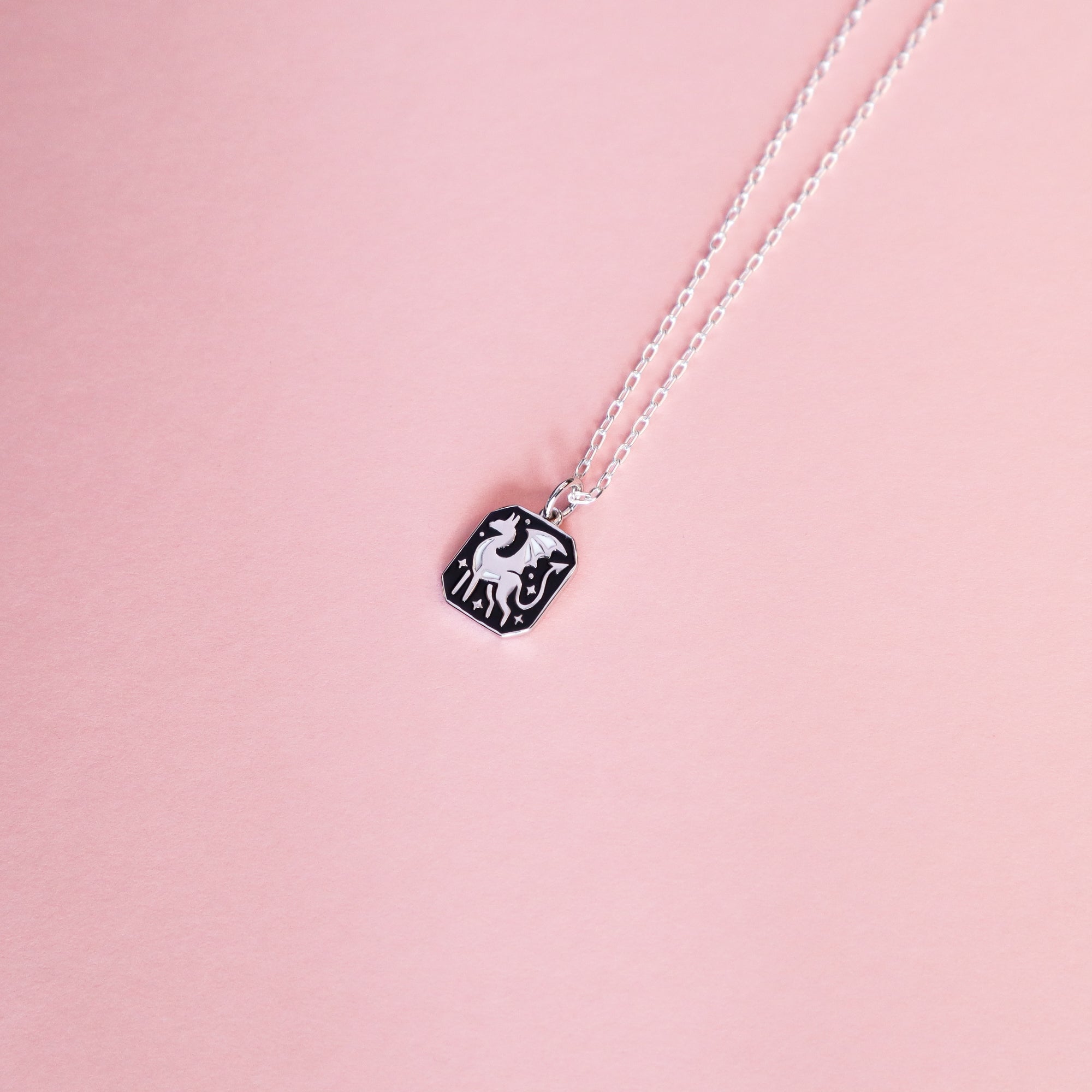 The Papio Press Silver Dragon Pendant Enamel Necklace features a rectangular black and white dragon design, displayed on a soft pink background.