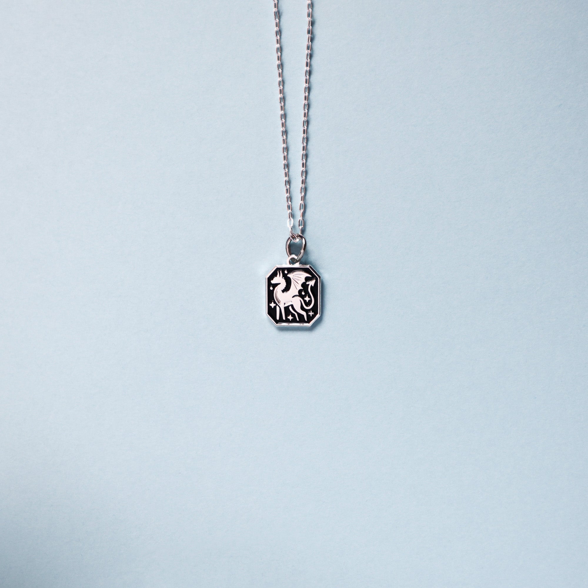 The Papio Press Silver Dragon Pendant Enamel Necklace, displayed against a light blue background, features a recycled silver hexagonal pendant with an engraved dragon design.