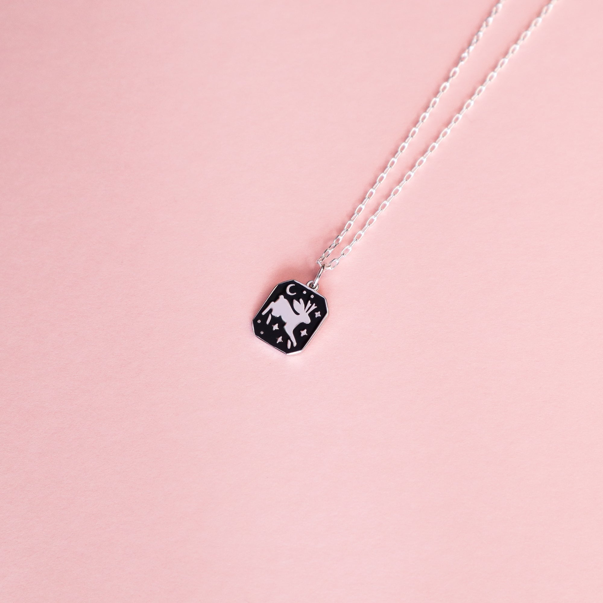 The Silver Jackalope Pendant Enamel Necklace by Papio Press features a black rectangular recycled silver pendant with a white mountain, moon, and stars design, displayed on a pale pink background.