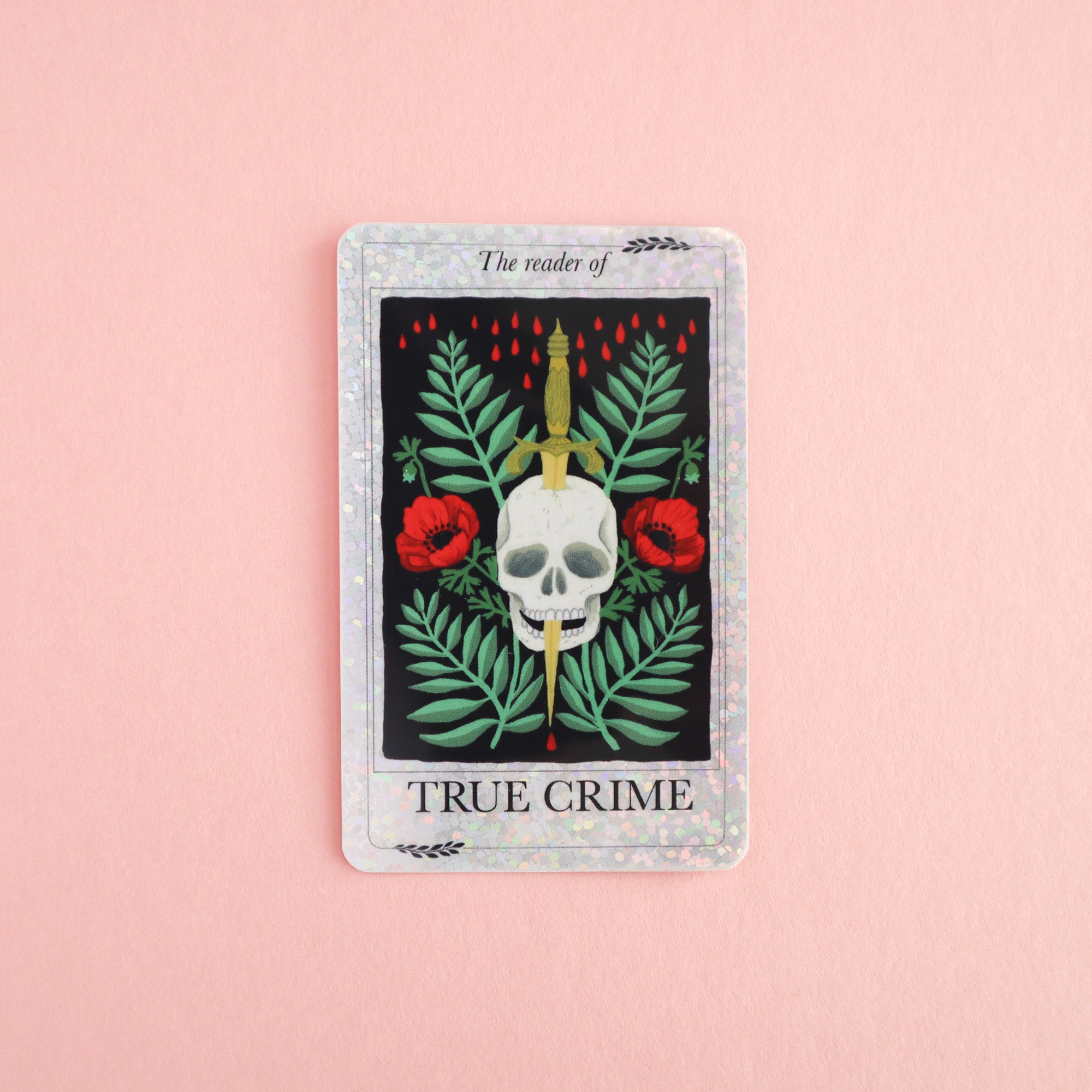 The Reader of True Crime Sticker by Papio Press is a tarot-inspired vinyl sticker with a skull, gold dagger, red flowers, and green leaves on pink. Glitter finish and The reader of TRUE CRIME text make it perfect for mystery lovers.