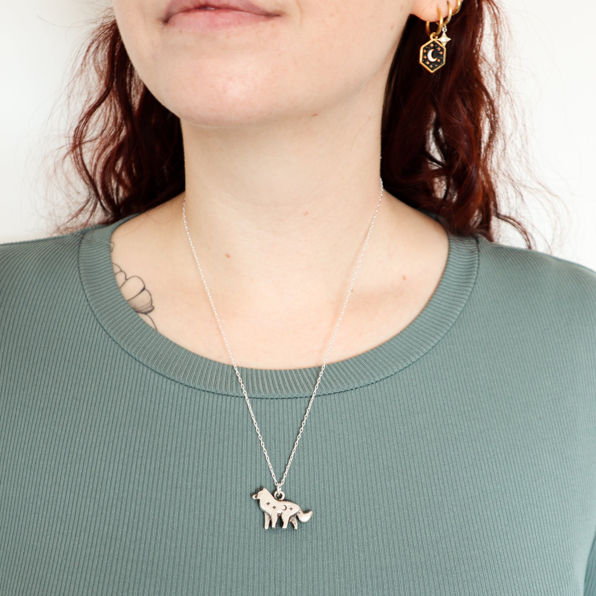 A woman with wavy reddish hair wears a green ribbed top, Papio Press's Silver Lunar Wolf Pendant necklace.