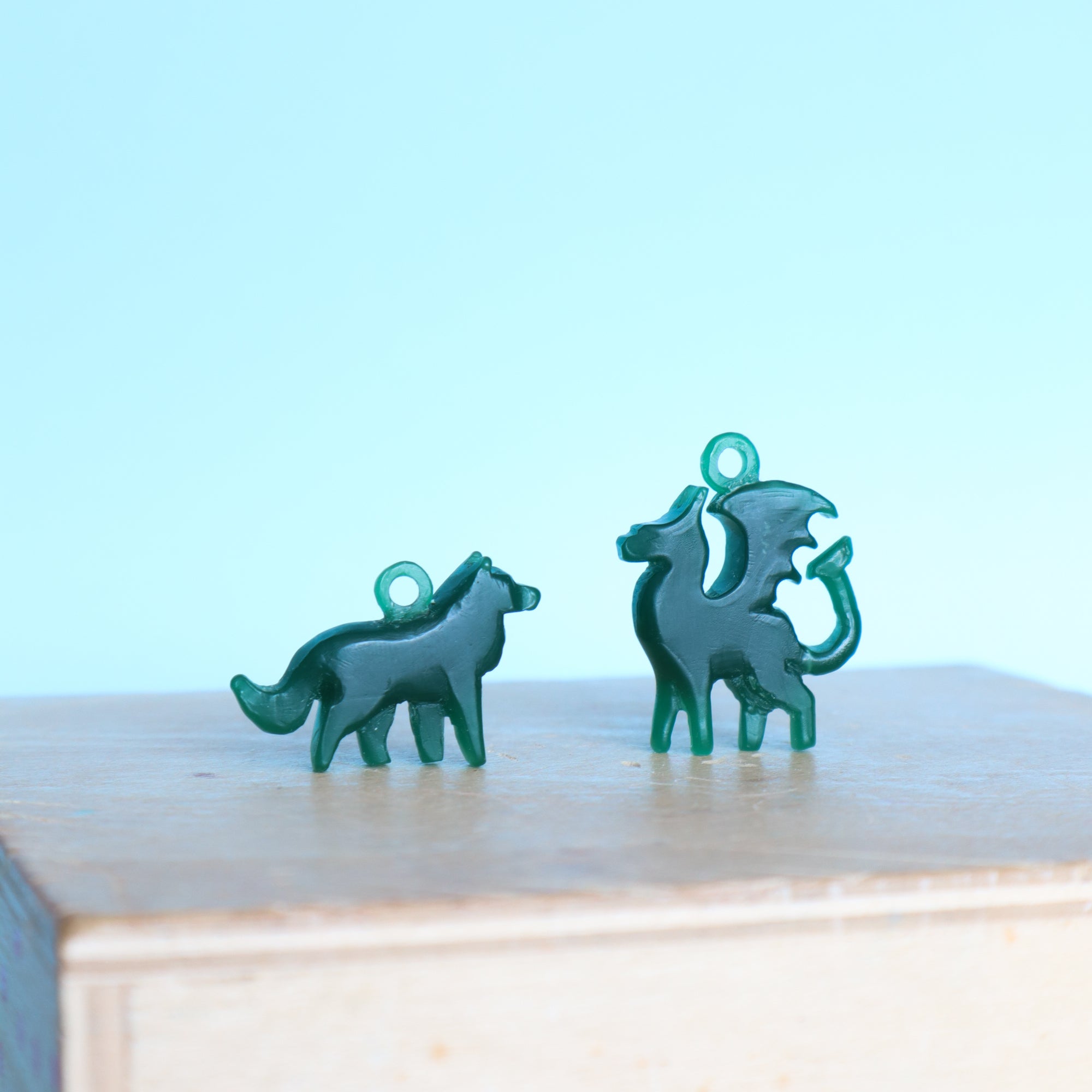 The original wax carvings of the Lunar Wolf and Dragon Pendants rests on a wooden surface.