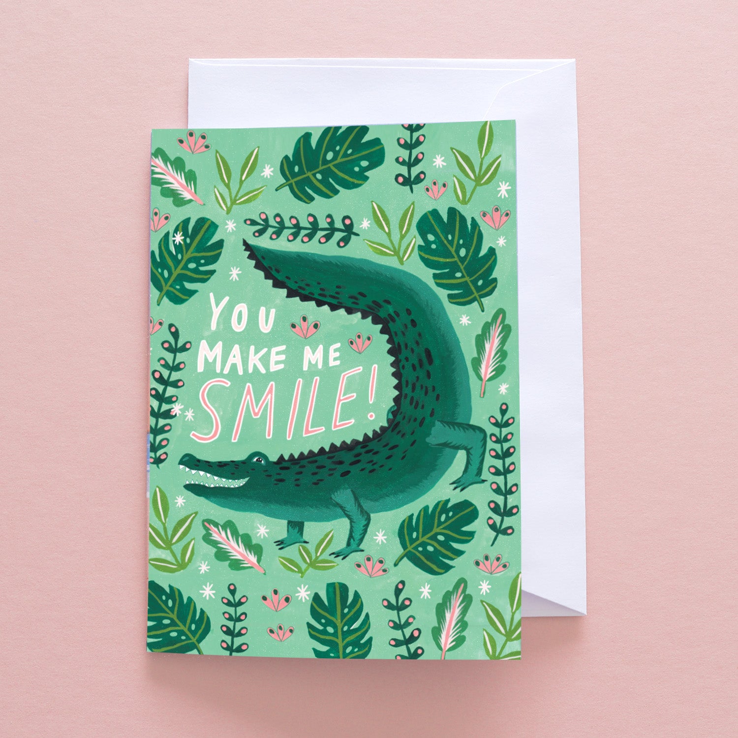 The Papio Press You Make Me Smile Crocodile Greetings Card showcases a green crocodile among leaves and flowers. Printed on recycled stock, it reads “You make me smile!” in playful lettering. Comes with a white envelope.