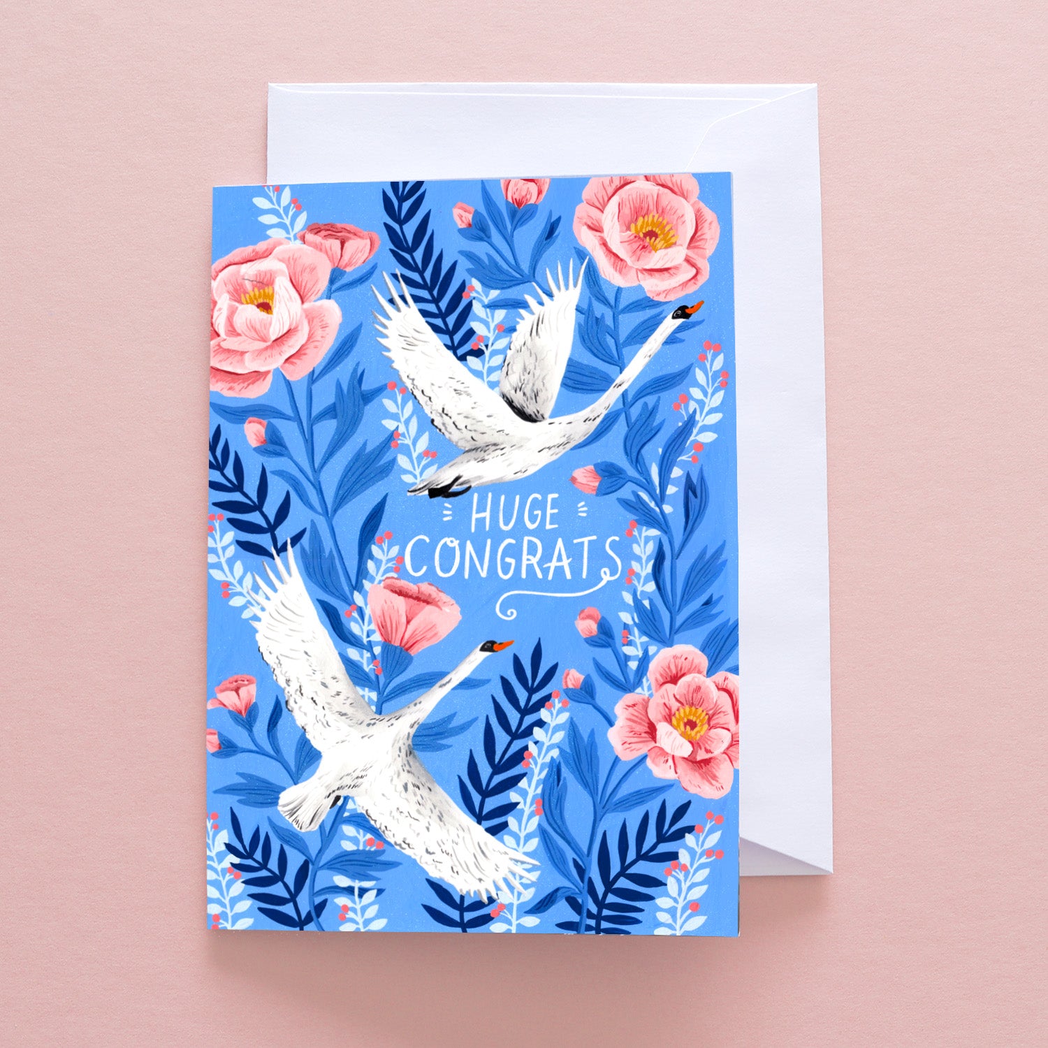 The Huge Congrats Swans Greetings Card by Papio Press features two white cranes among pink flowers and blue leaves on a blue background, with “Huge Congrats” text. Printed on recycled stock and supplied with a white envelope.