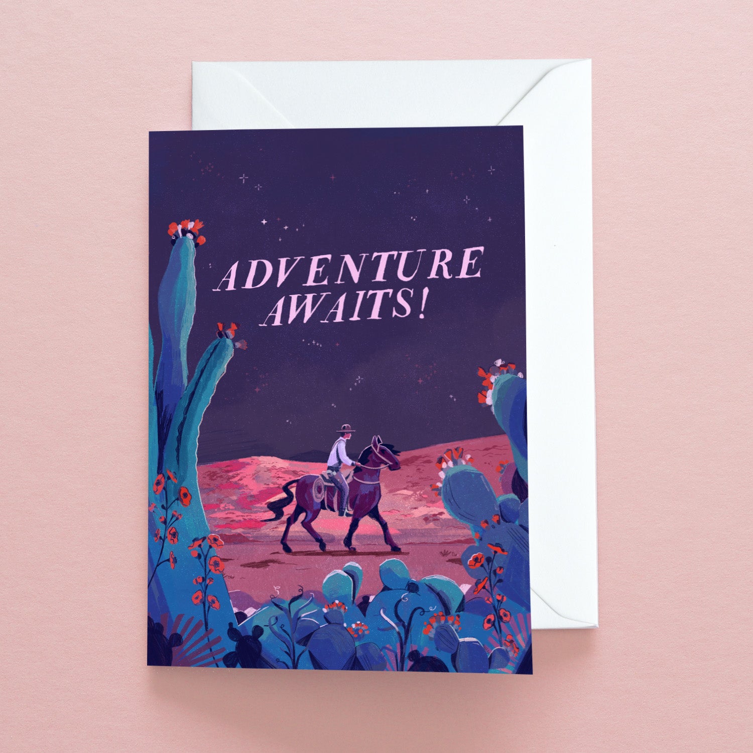 The Papio Press Adventure Awaits Cowboy Greetings Card features a cowboy riding through a desert with cacti and flowers under a night sky, with ADVENTURE AWAITS! in bold white letters, printed on recycled stock.