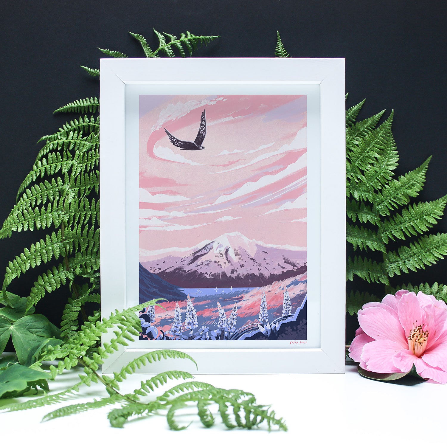 The Papio Press Mt. Cook National Park, New Zealand Artists Print features a snow-capped mountain, pink sky, and bird, framed by green ferns and a pink flower on black. Printed on archival satin paper for vibrant longevity.