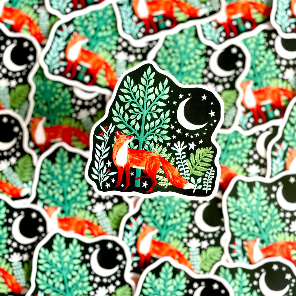 A photograph of a pile of vinyl fox stickers. The Fox is looking up at a moon and is standing in front of a green tree. 