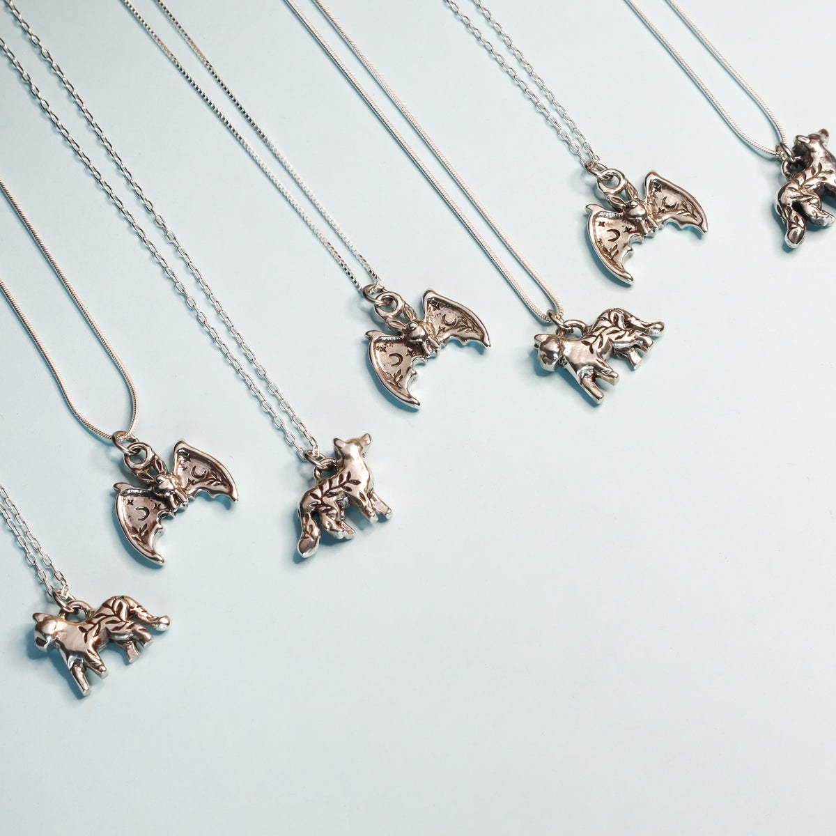 A selection of silver pendants featuring a bat, a fox and a cat on a light blue background. 