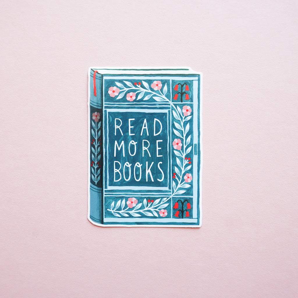 A picture of a book sticker that says 'Read More Books'. The photo is taken on a pink background.