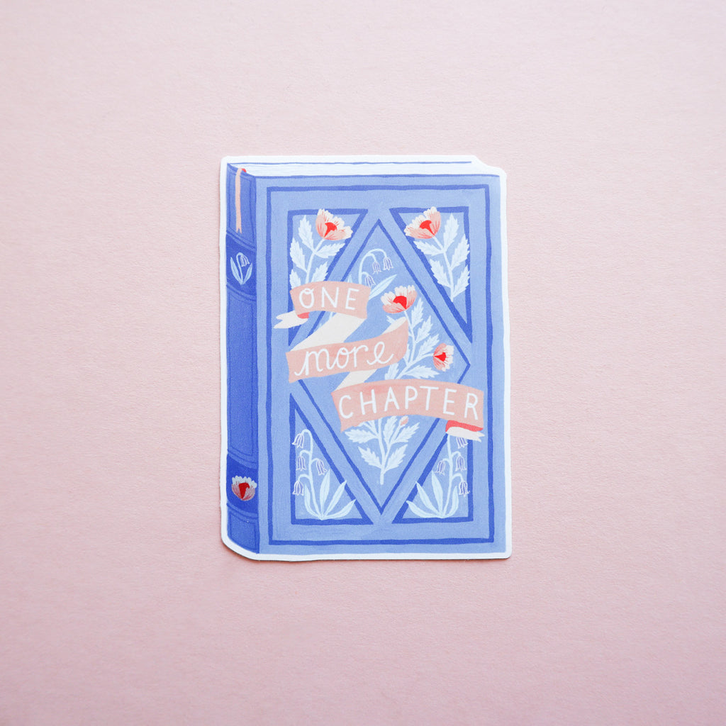 A picture of a book sticker that says 'One more Chapter'. The photo is taken on a pink background.