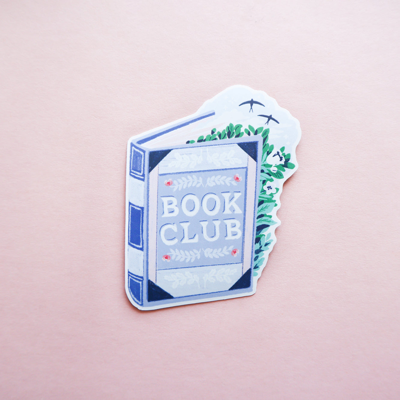 The Book Club Book Sticker by Papio Press features a blue book with BOOK CLUB on the cover, surrounded by green leaves and birds on a soft pink background—a perfect durable vinyl sticker for any book lover.