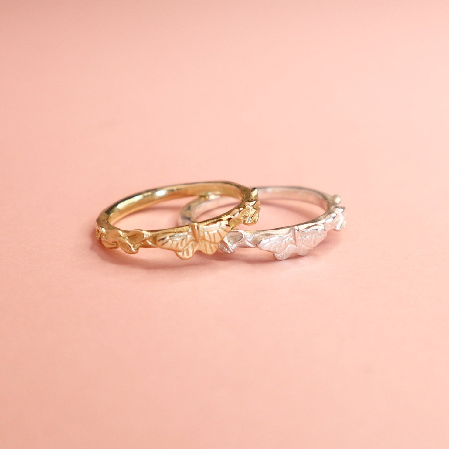 Two butterfly rings, one gold and one silver on a light pink background. 