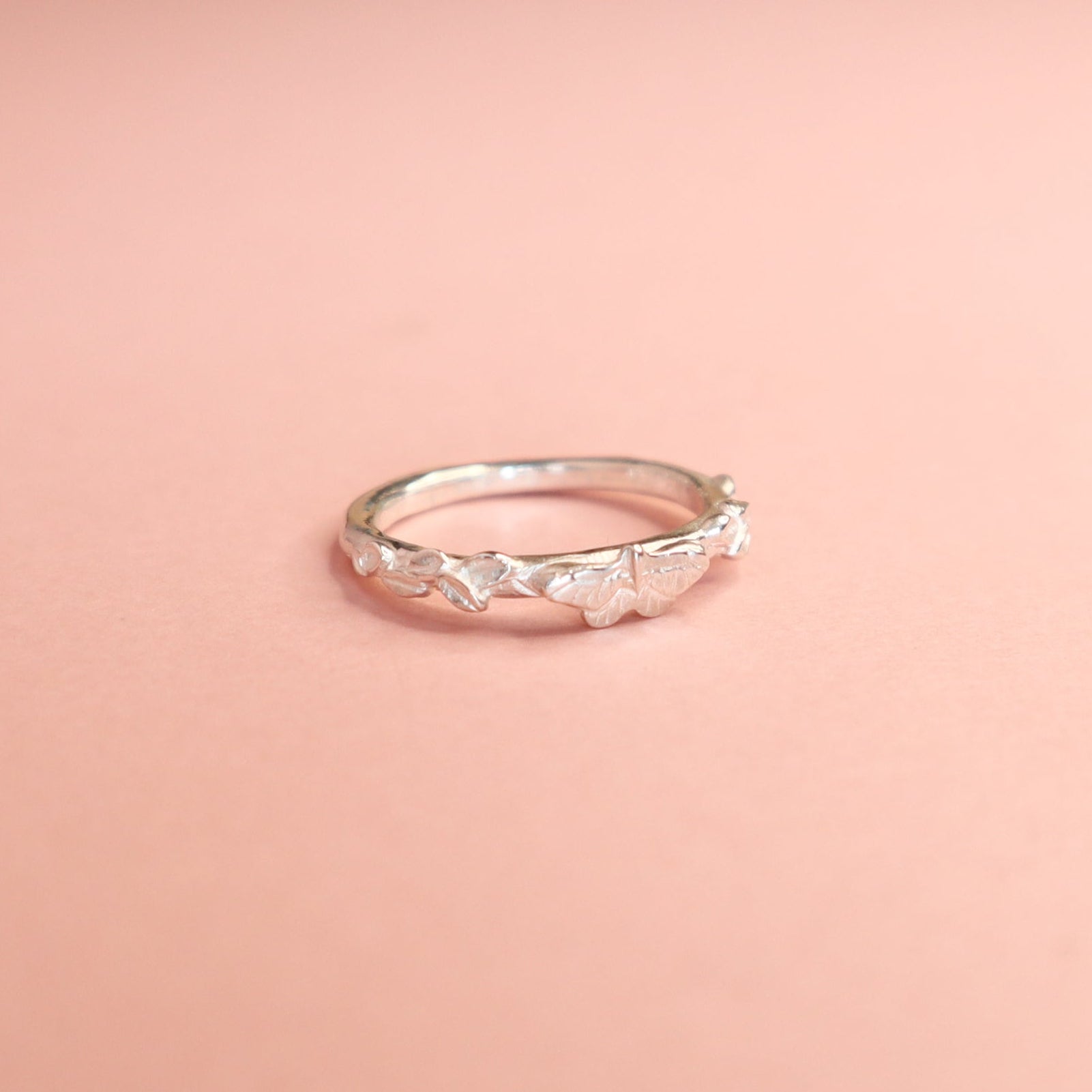 A silver butterfly ring on a light pink background. 