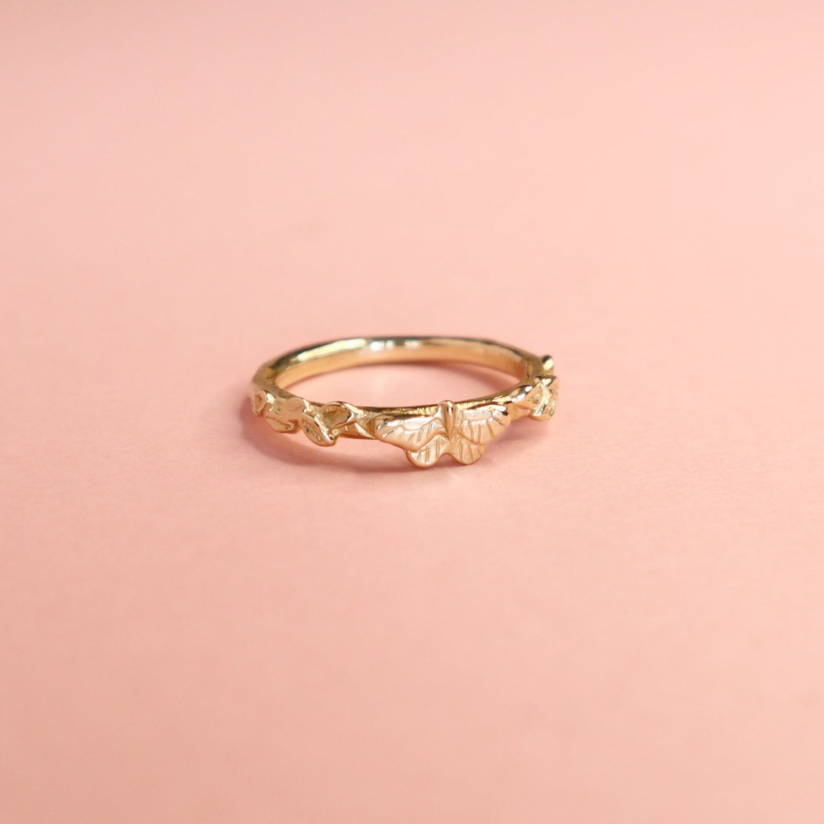 A gold butterfly ring on a light pink background.