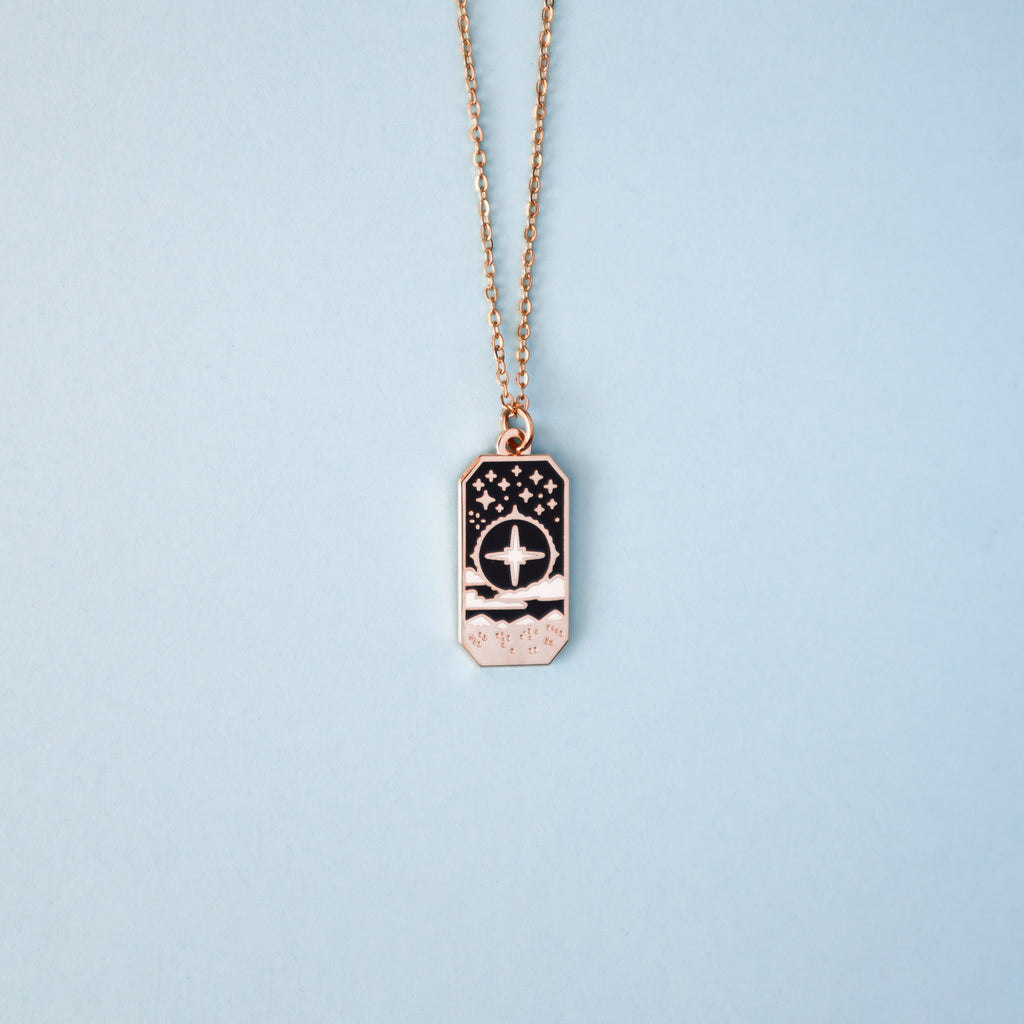 A gold Cleric necklace on a light blue background. 
