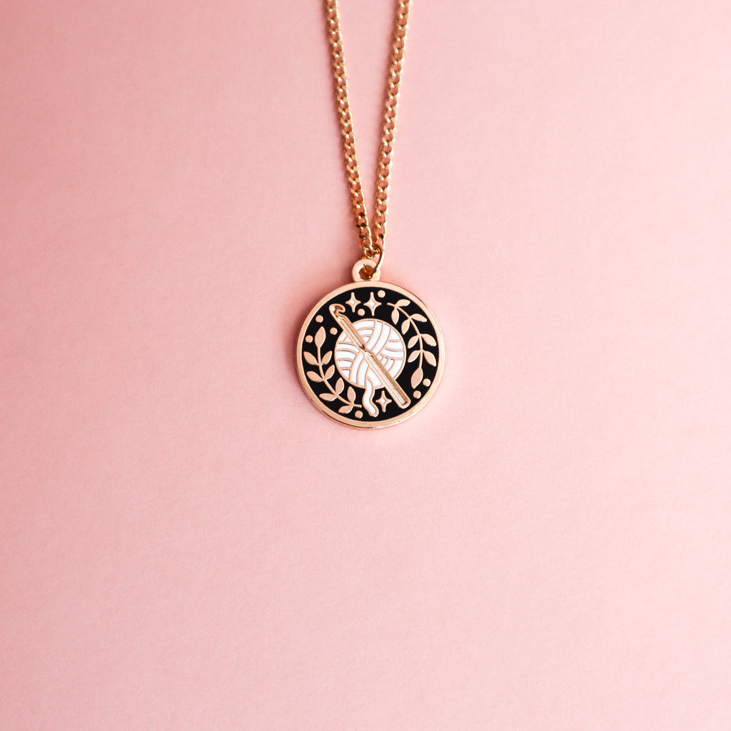 A gold crochet necklace on a pink background.