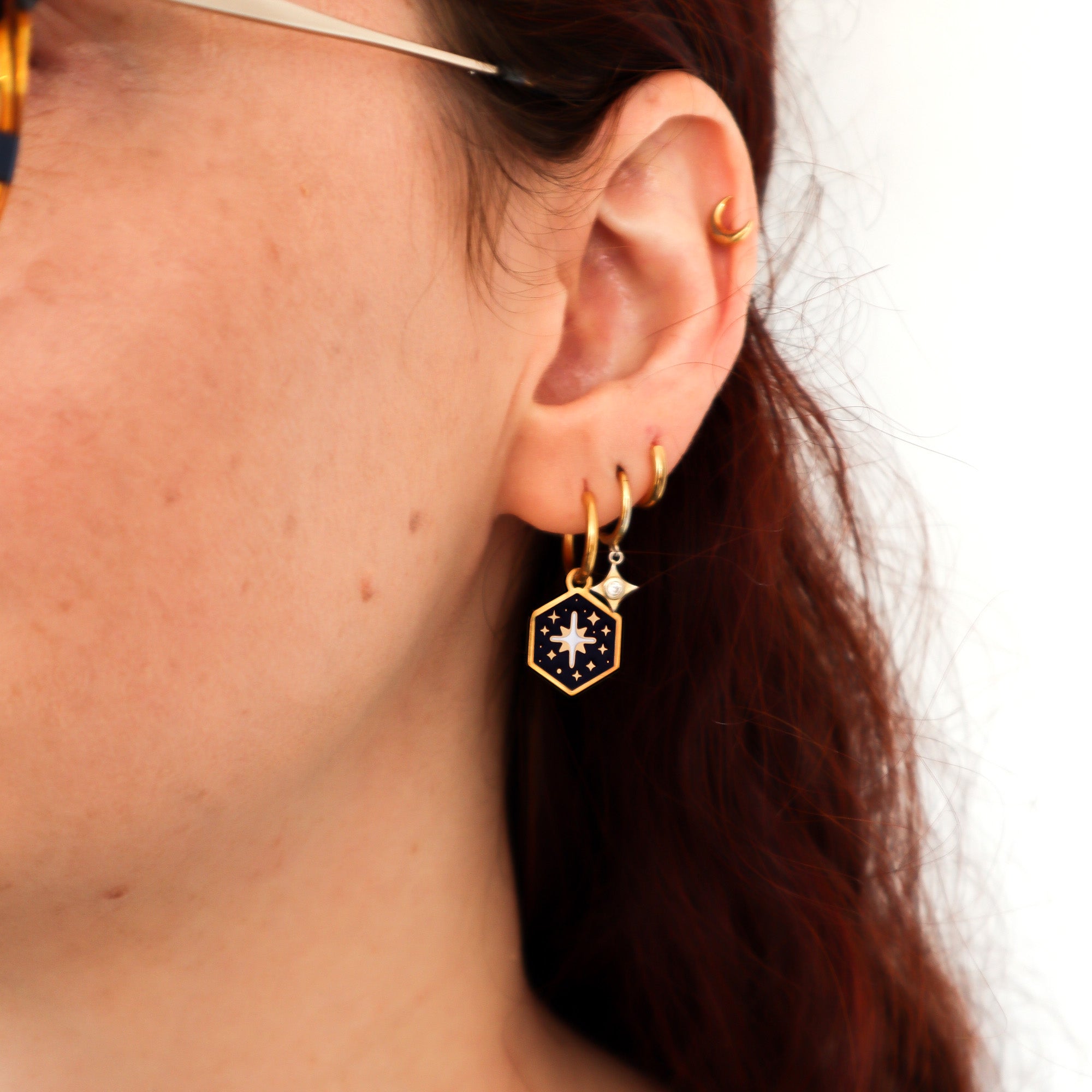 A person with long, reddish-brown hair wears multiple gold plated earrings, including Papio Press Mix and Match Mini Hexagon Earrings.